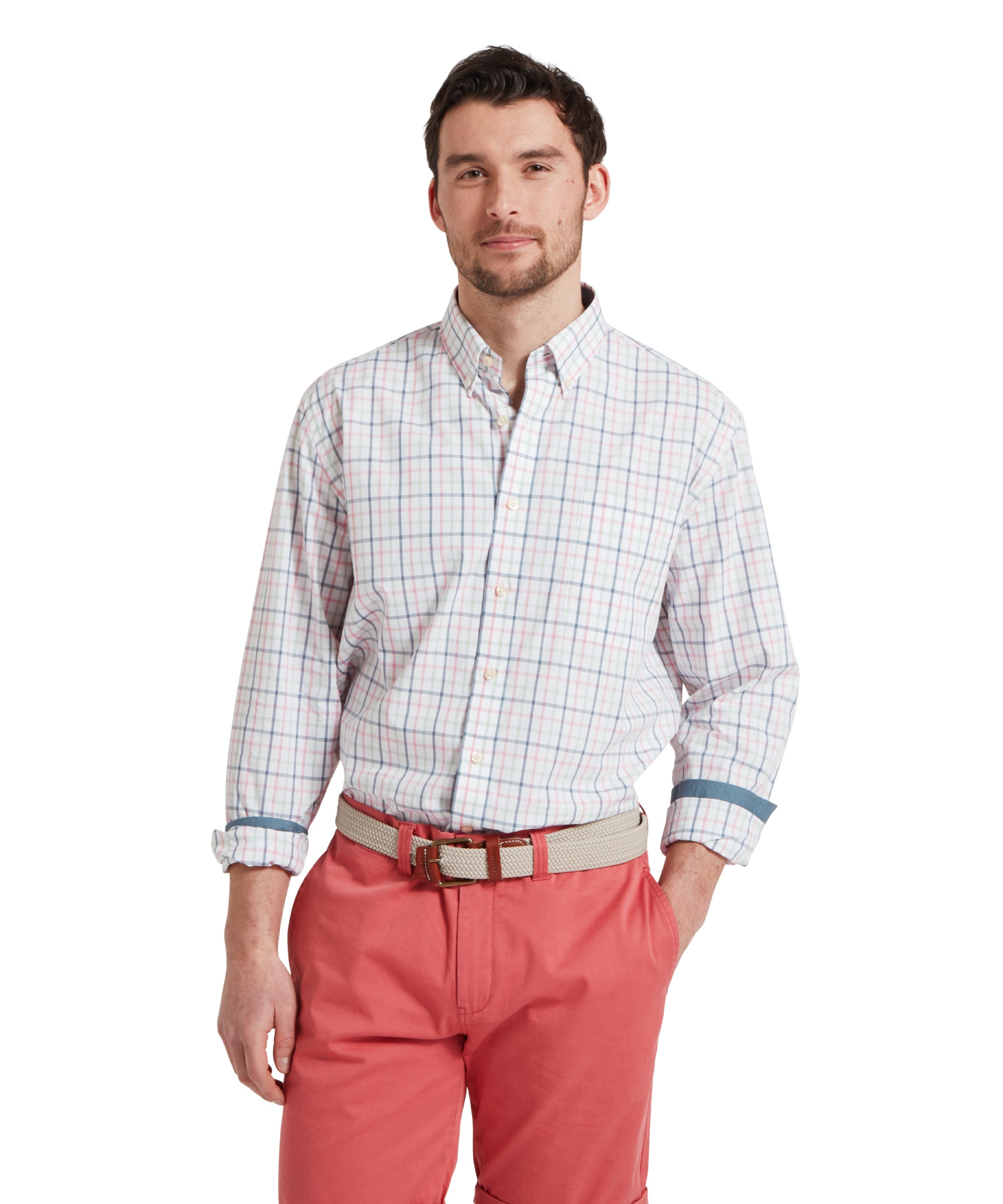 A man wears the Schöffel Holkham Classic Shirt for Men in Blue and Pink with the collar open and the sleeves rolled up slightly. He has partnered with coral shorts and a beige woven belt. He has his left hand placed in his jeans pocket.