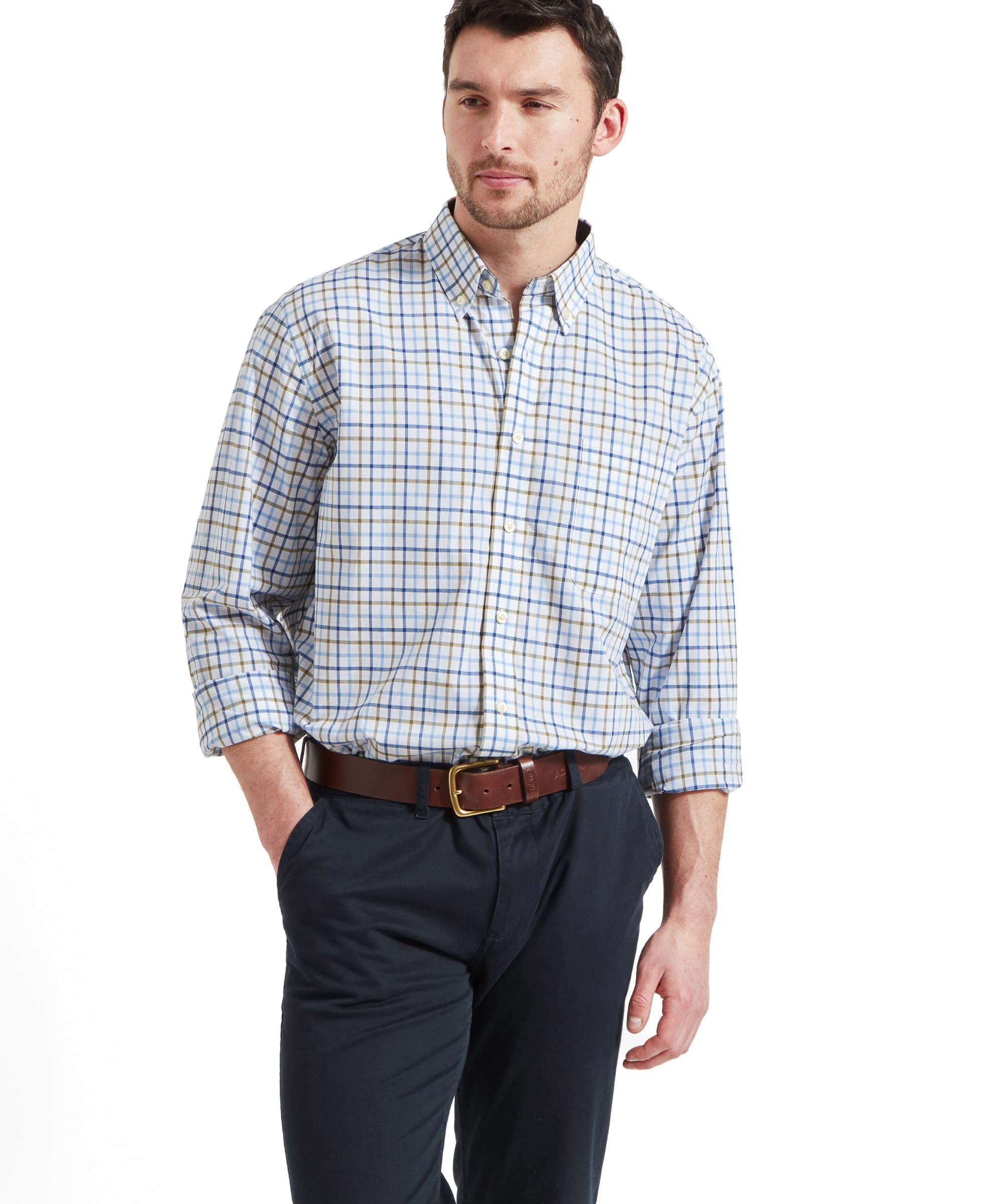 A man wears the Schöffel Holkham Classic Shirt for Men in Navy with blue trousers and a brown leather belt. He has his left hand in his pocket and the shirt sleeves are rolled up his forearms.