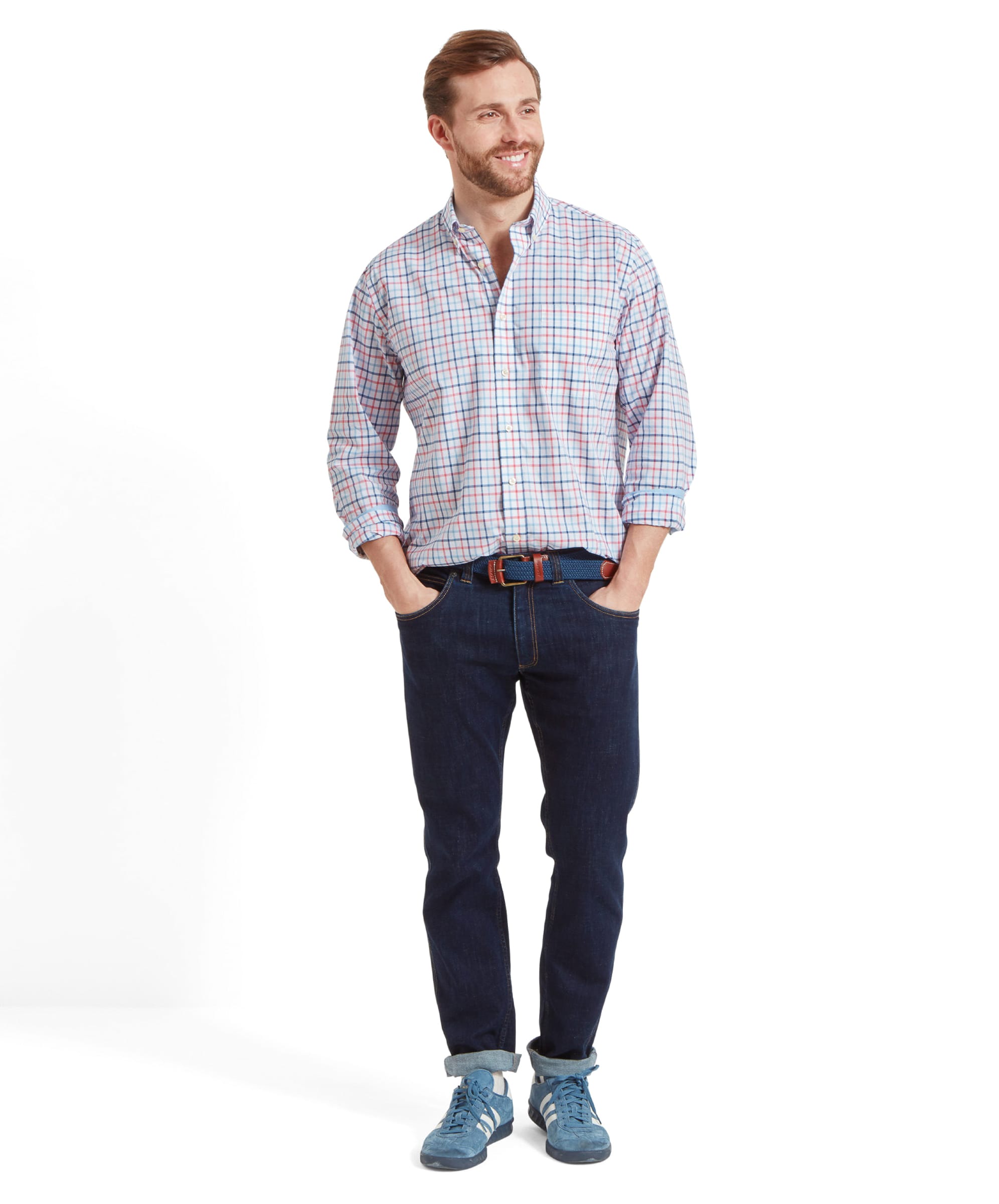 Full body view of the same man wearing the Schöffel Holkham Classic Shirt for Men in Navy and Red with both hands in his pockets. He wears with dark navy jeans, a blue woven belt and light blue trainers.