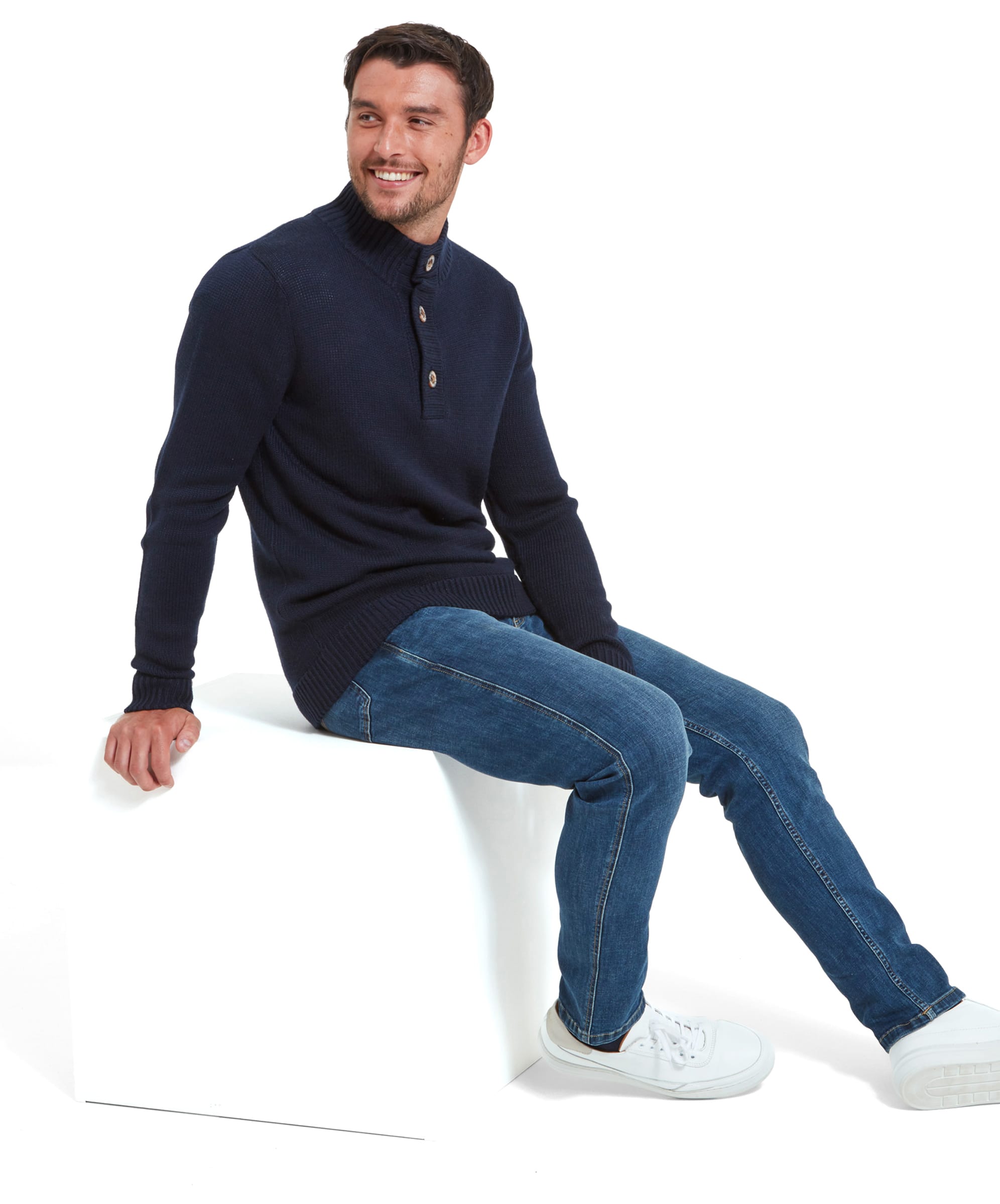 Side view of a man wearing the Schöffel Kenmore Lambswool Mix Jumper for Men in Navy and wears it with denim jeans and white trainers. He is looking over his left shoulder.