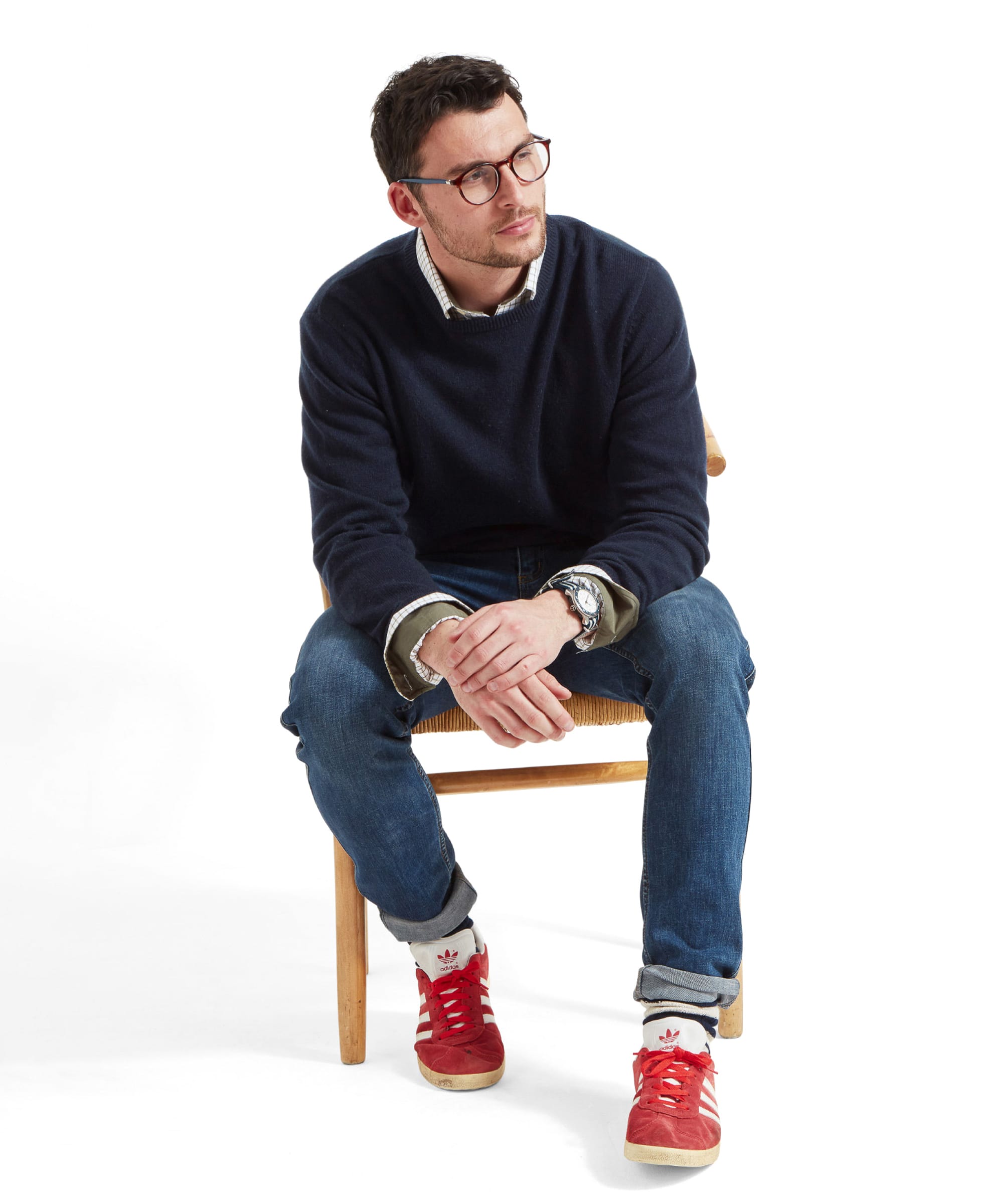 Another whole outfit shot of the model sitting on a wooden chair whilst leaning forward, wearing the Schöffel Lambswool 1/4 Zip for Men in Navy