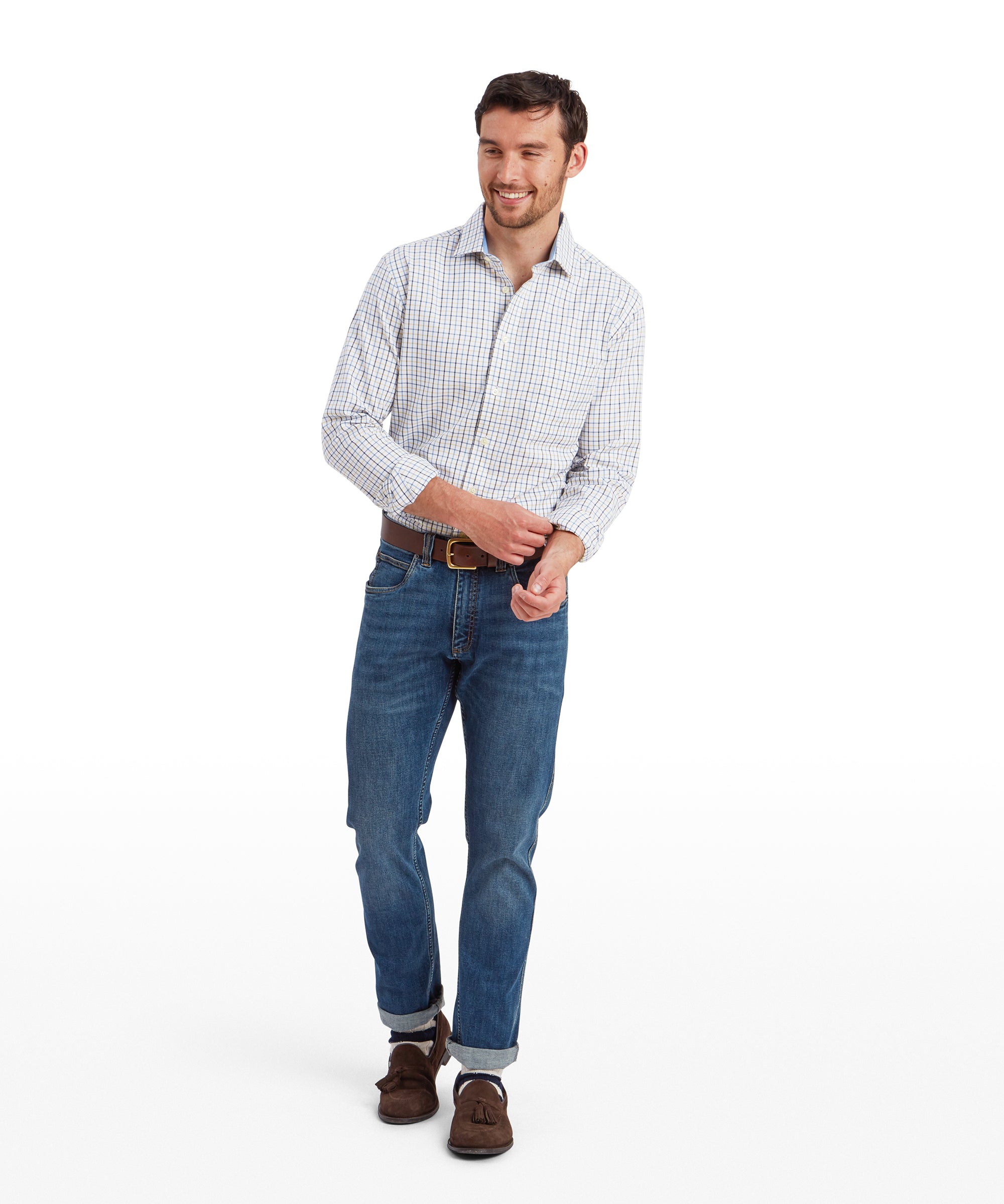 A full-body shot of the same man wearing the Schöffel Milton Tailored Shirt for Men in Blue and blue jeans. He is smiling and adjusting the cuff of his left sleeve with his right hand. His jeans are paired with brown suede loafers, and he is wearing a brown leather belt. The background is plain white, keeping the focus on the outfit.