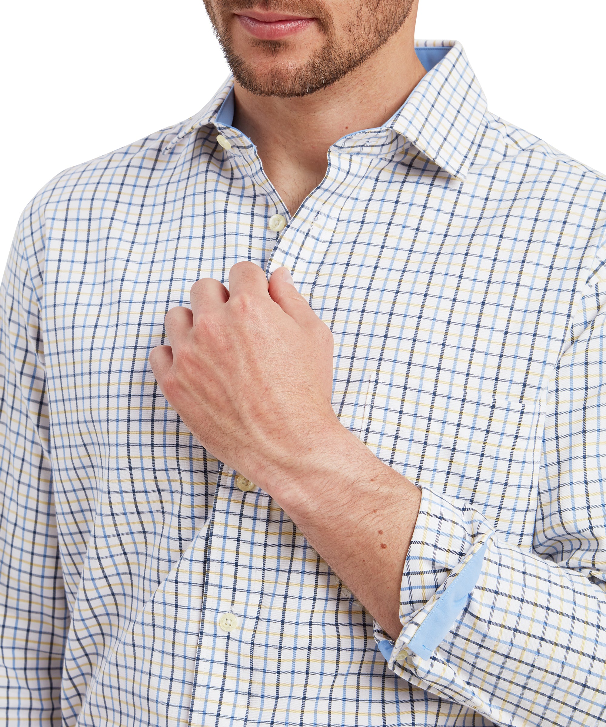 A close-up of the man’s upper torso, focusing on the details of the Schöffel Milton Tailored Shirt for Men in Blue. He is lightly holding the shirt near his chest, emphasising the shirt’s buttoned placket and the subtle blue lining inside the collar. The blue, yellow, and white checkered pattern is clearly visible. The shirt's cuffs are rolled up slightly, revealing the blue lining on the inside.