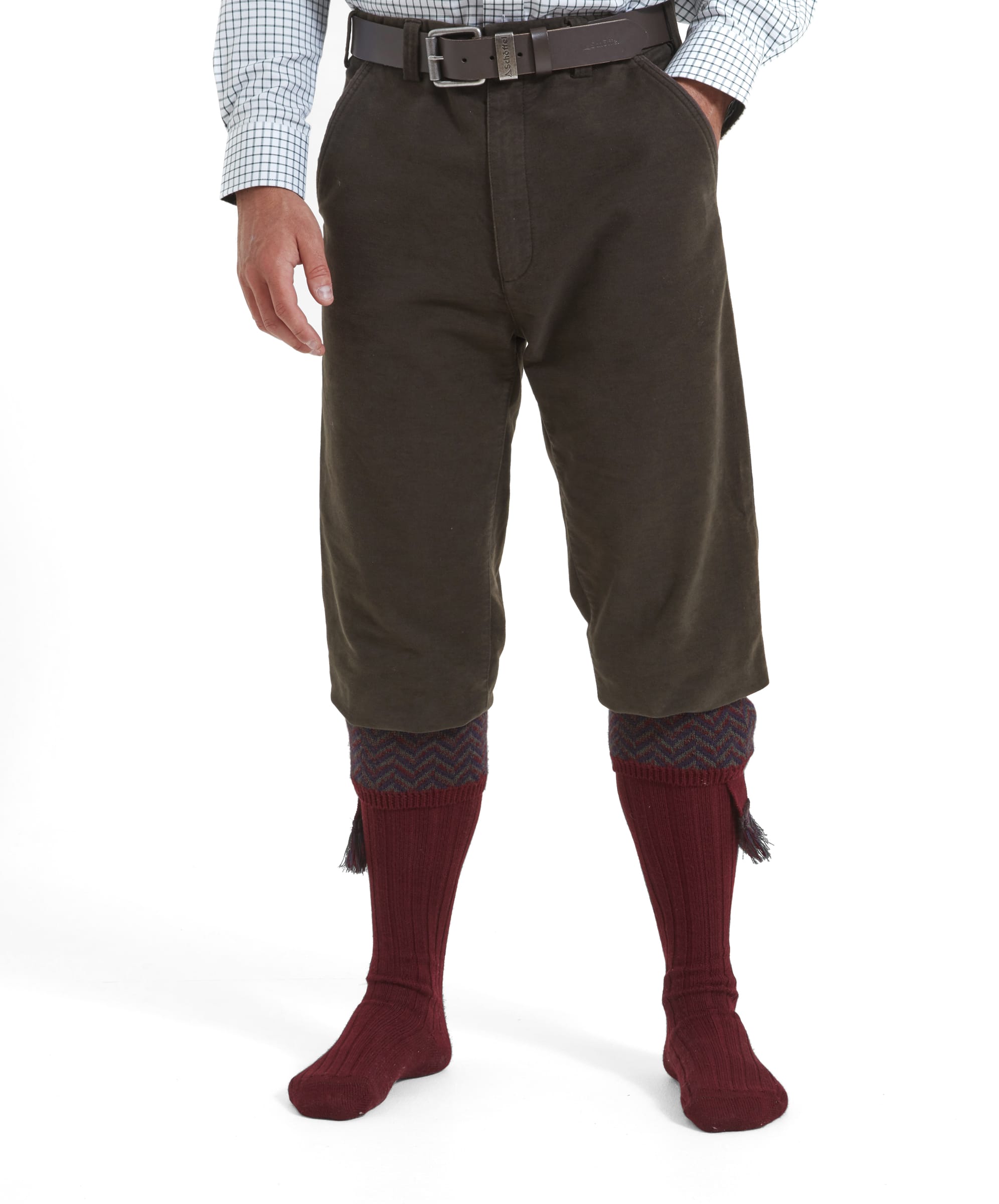 A model wears the Schöffel Moleskin Trousers for Men in Green with tall burgundy tassled shooting socks and a navy check shirt and a dark brown leather belt. The fit on the trousers is loose and they sit just below the knee.