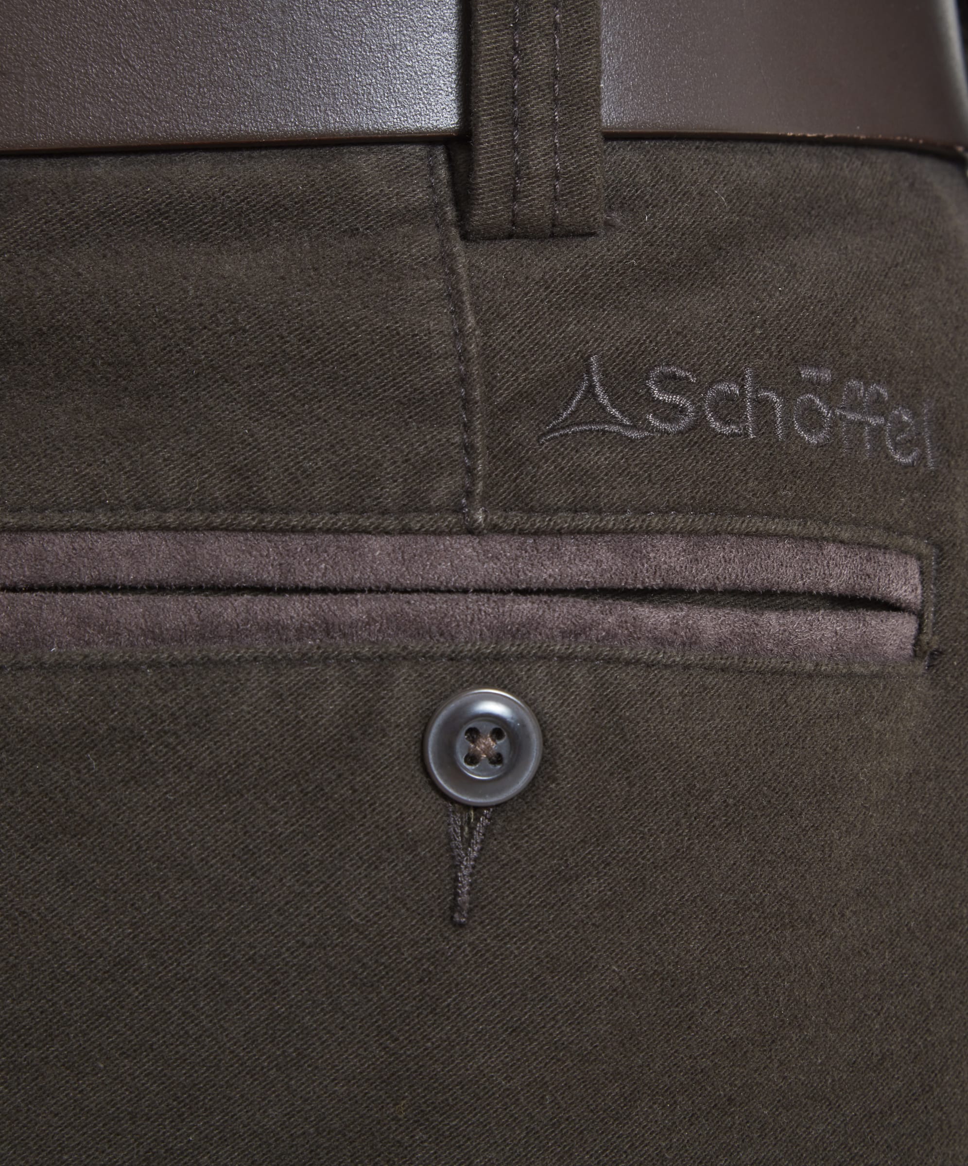 A close-up view of the back pocket on the Schöffel Moleskin Trousers for Men in Green highlighting the woven brown fabric and a suedette finished edge to the pocket. A small button fastens the pocket closed so items don't fall out and the Schöffel logo has been embroidered just above the right pocket in a tonal brown thread.