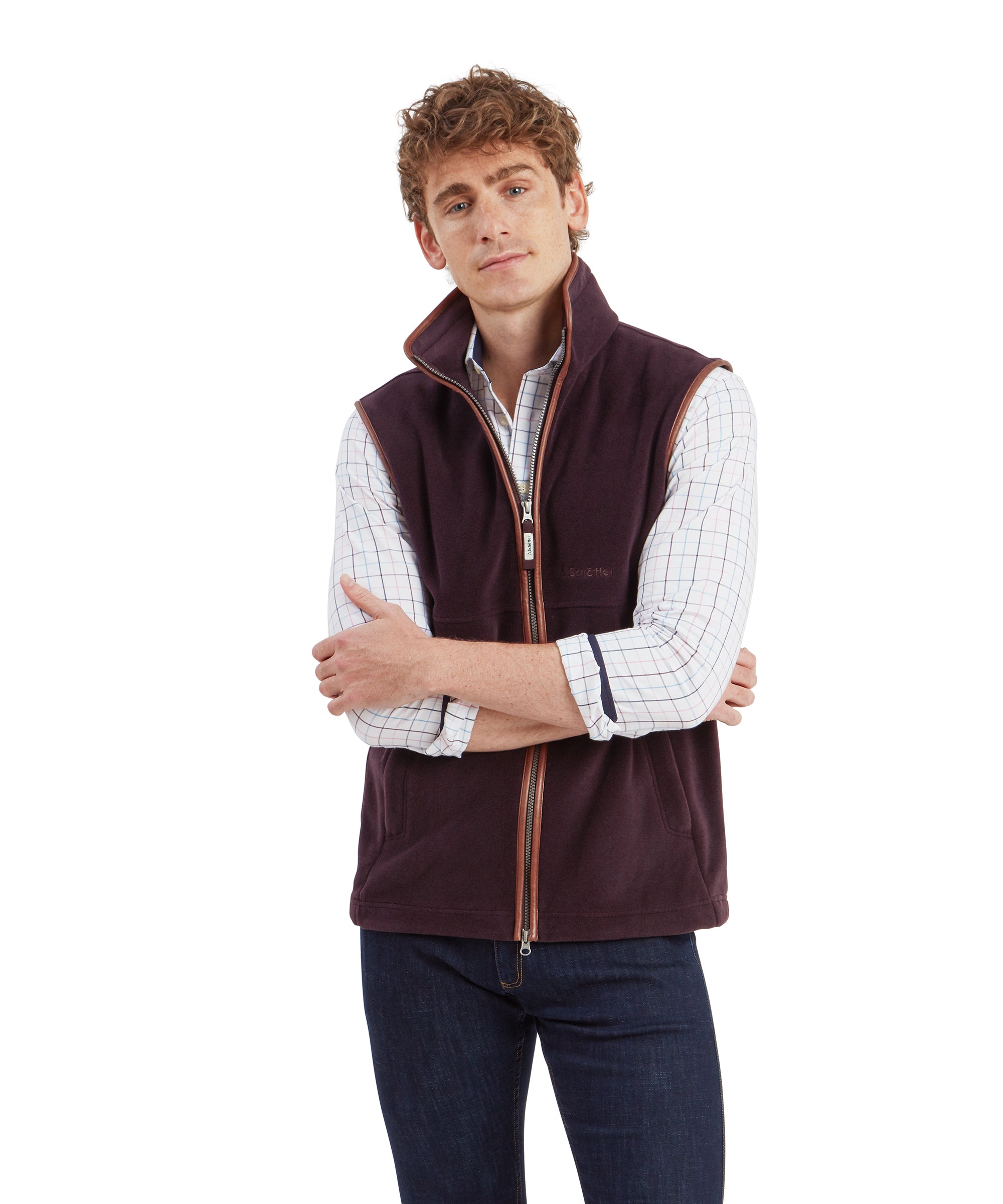 A man wears the Schöffel Oakham Fleece Gilet for Men in Brown with a light blue and purple check shirt and dark denim jeans. He holds his arms folded across his chest and a cheeky expression.