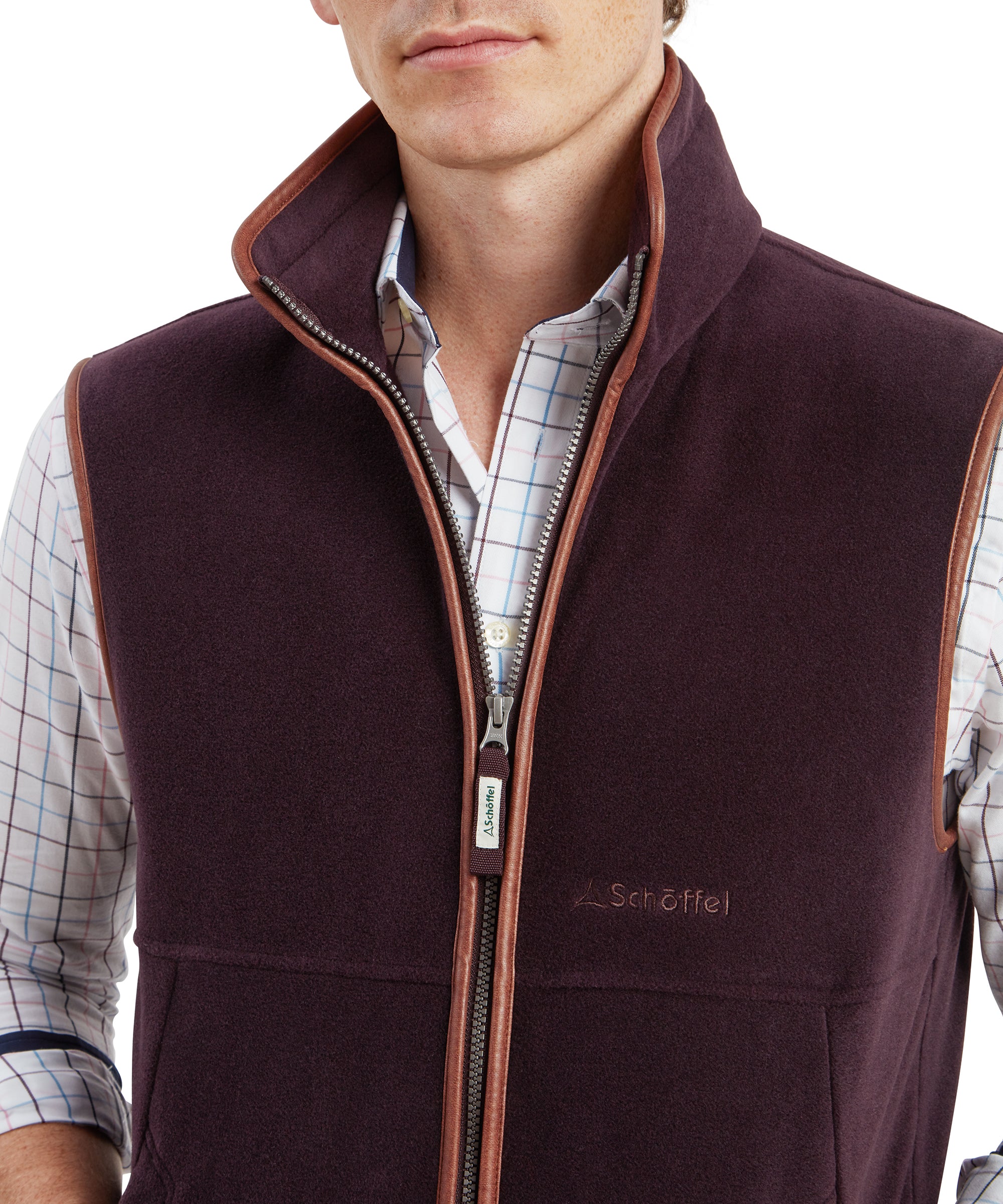 Close-up view of the zip and collar area on the Schöffel Oakham Fleece Gilet for Men in Brown highlighting the Schöffel branded zip pull featured in a tonal purple brown fabric to match the gilet colour. The collar is tall and sits just under the mans jaw line and the faux leather trim is along all edges. A small embroidered Schöffel logo can be seen on the right chest area in a tonal brown thread.