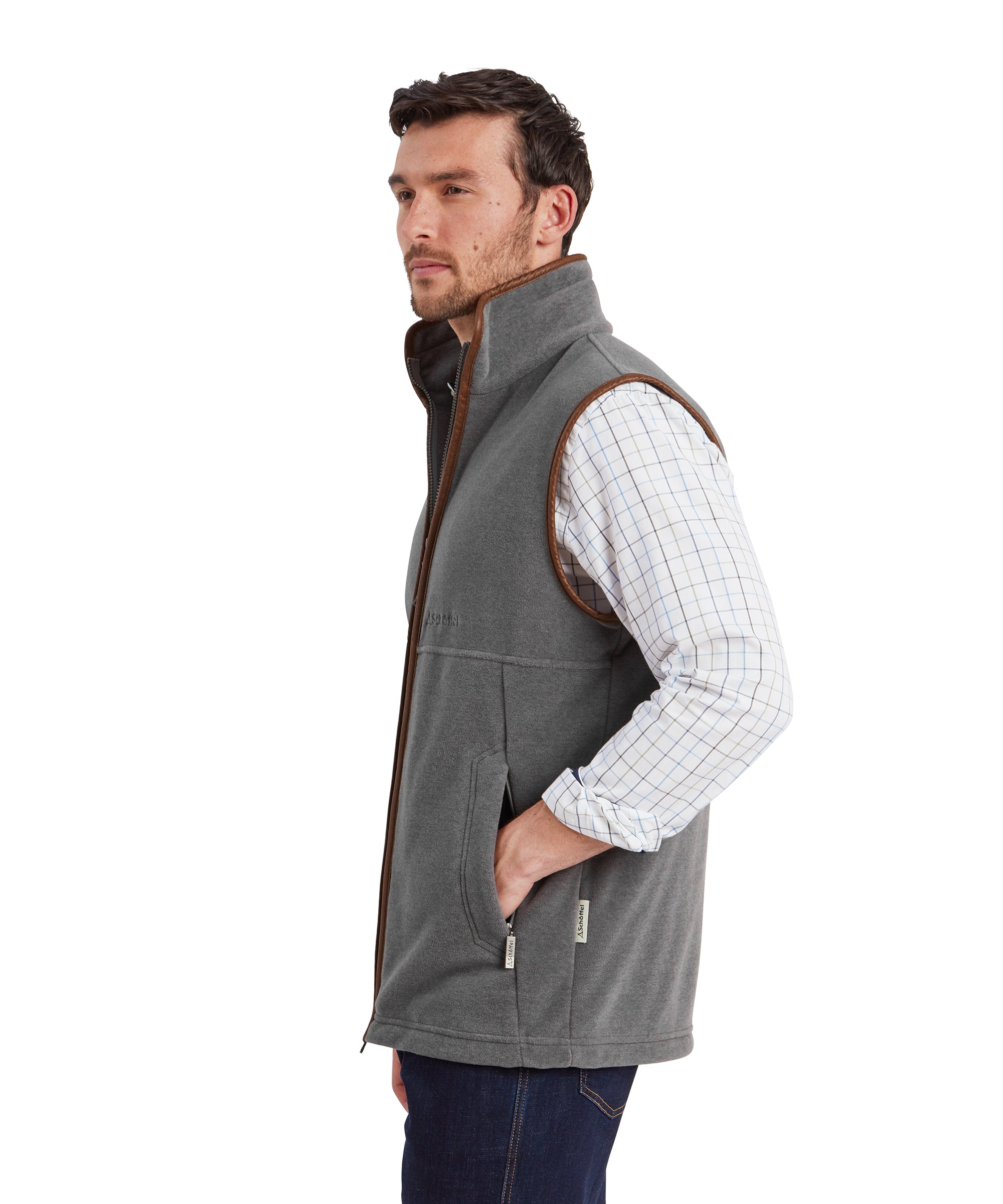 A side view of the male model wearing the Schöffel Oakham Fleece Gilet for Men in Light Grey partnered with a same long sleeve checked shirt and dark denim jeans. The fit and design of the gilet can be seen clearly with the faux leather brown trimmings and the pocket design.