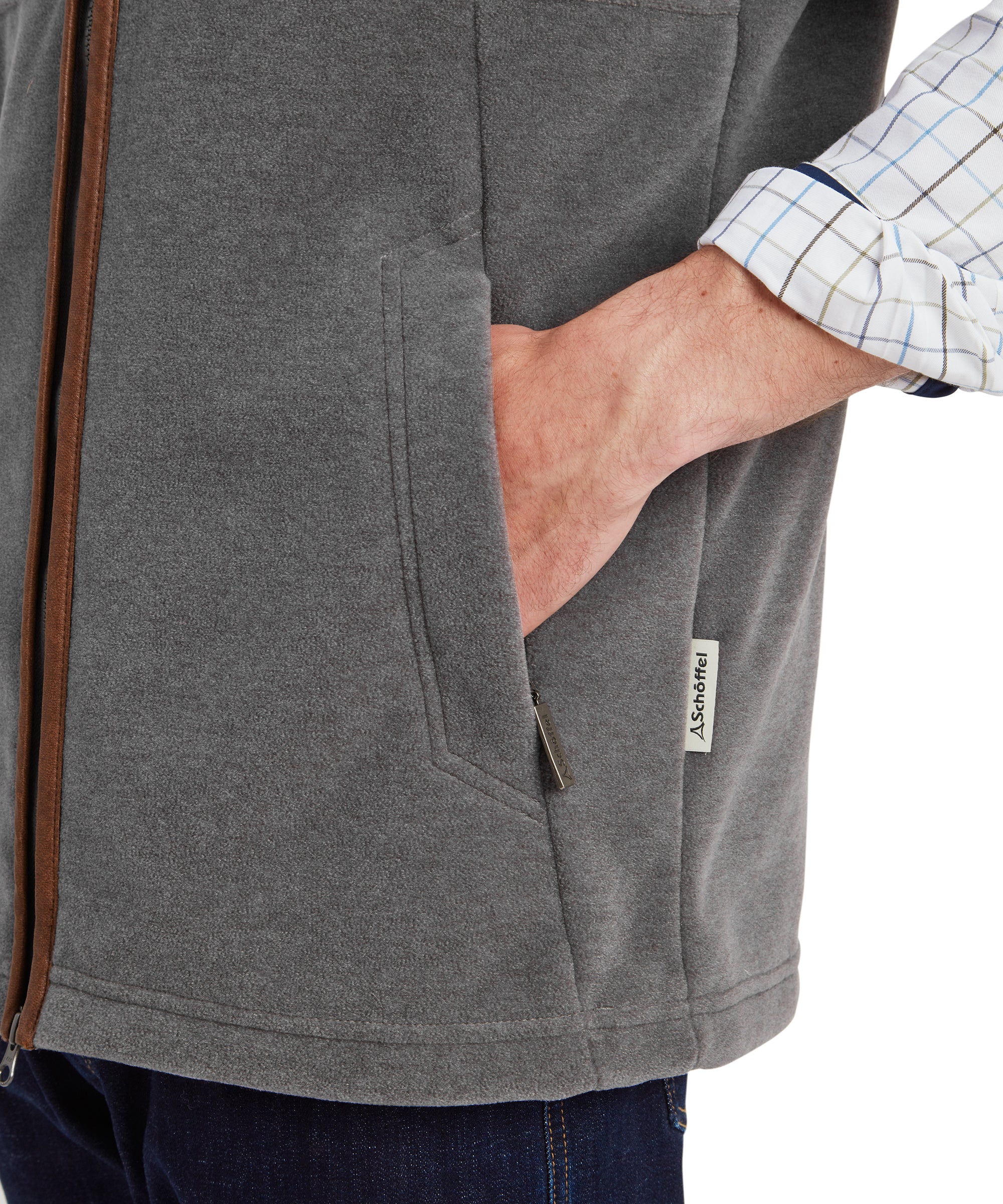 Close-up on the front pocket on the Schöffel Oakham Fleece Gilet for Men in Light Grey highlighting the double stitching design and the metal zip pull on the pocket zipper. The man holds his hand in the pocket to show the generous size. Down the side seam a Schöffel branded pip can be seen.