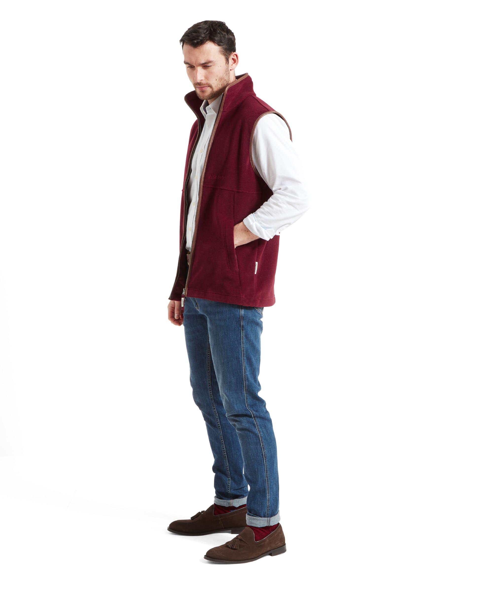 The model is standing with one hand in the pocket of the Schöffel Oakham Fleece Gilet for Men in Red, highlighting its practical pockets.