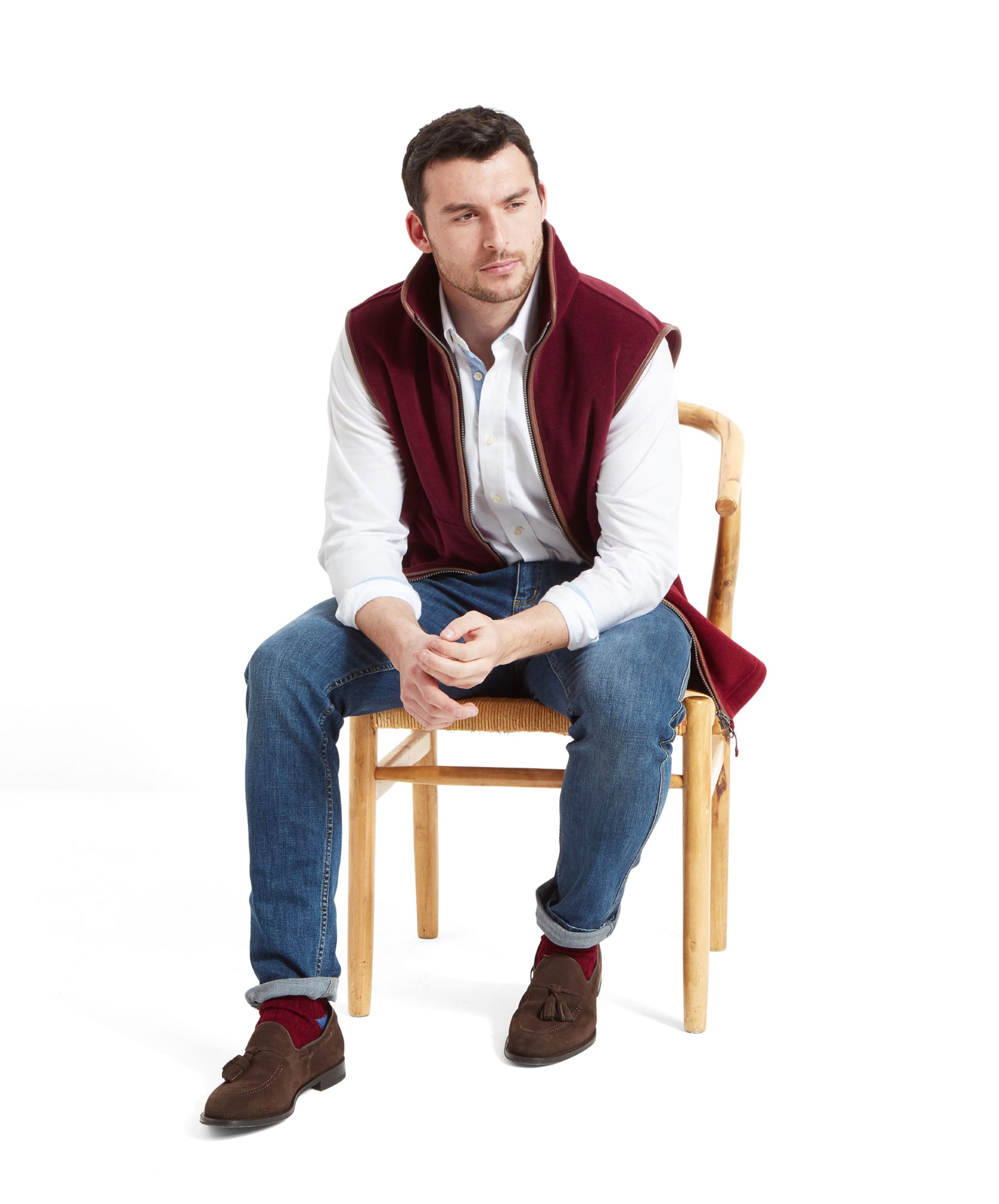 Seated comfortably, the model looks off to the rightside while wearing the Schöffel Oakham Fleece Gilet for Men in Red.