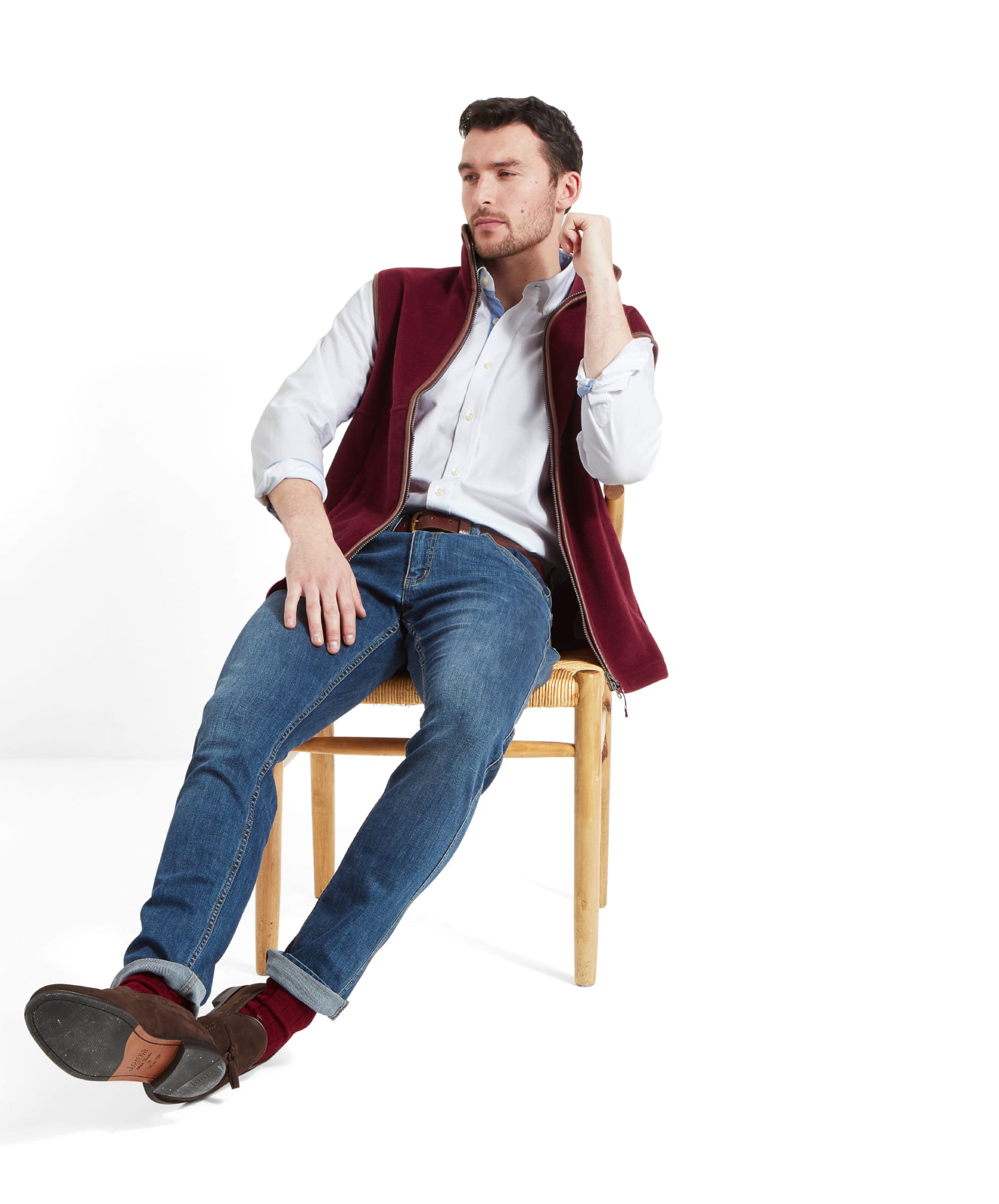 Seated comfortably, the model looks off to the left side while wearing the Schöffel Oakham Fleece Gilet for Men in Red.