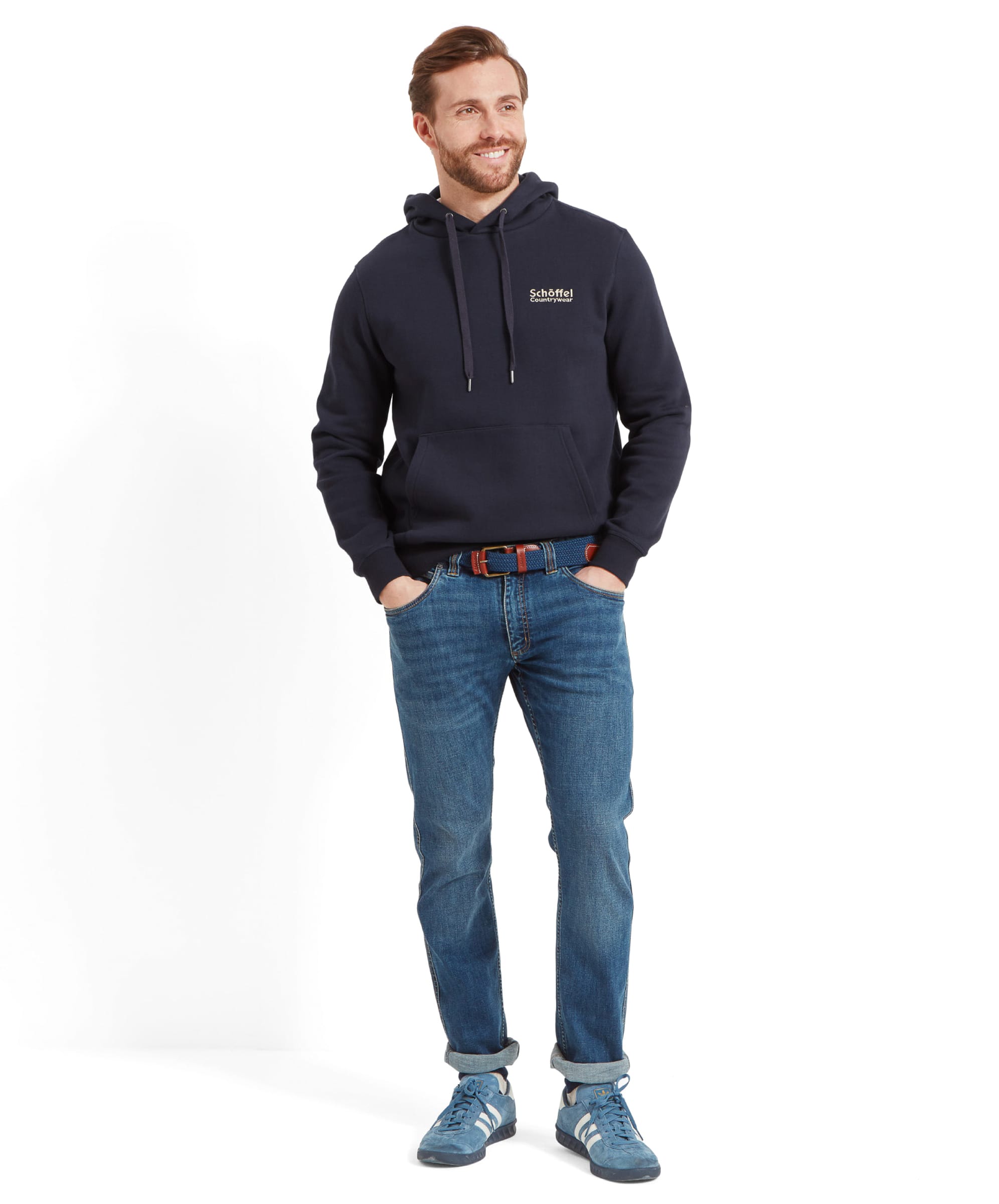 The man stands casually with a smile, showcasing the Schöffel Pentire Heritage Hoodie for Men in Navy. He pairs the hoodie with jeans and casual shoes, giving a relaxed and comfortable look.