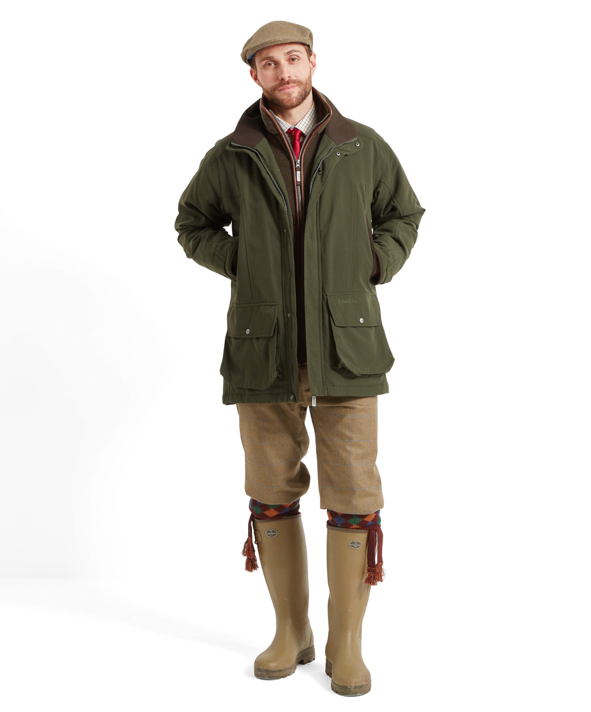 Full-body shot of a man wearing the Schöffel Ptarmigan Classic Coat for Men in Green, paired with traditional attire including a hat, tweed breeks, and wellington boots, hands in pockets, standing in a confident posture.