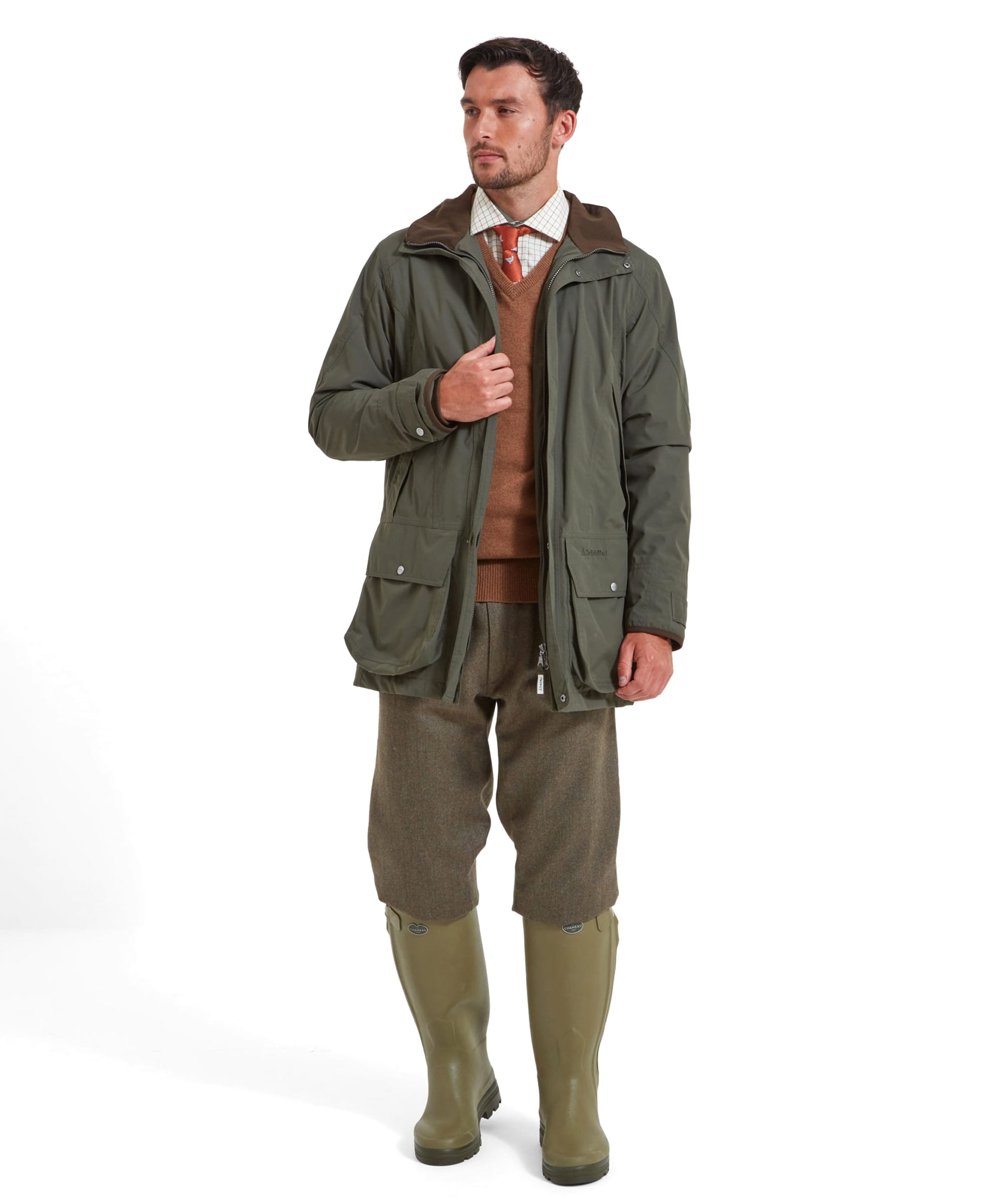 Full body view of a man in the Schöffel Ptarmigan Ultralight II for Men in Green with tweed trousers, an orange jumper and rubber wellington boots.