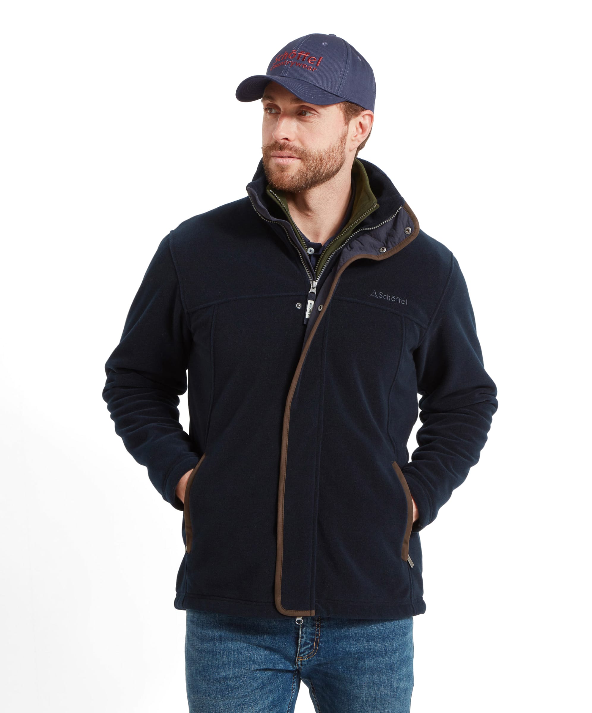 A man models the Schöffel Rutland Fleece for Men in Navy with his hands in his pockets. He wears it with a navy blue cap and denim jeans.