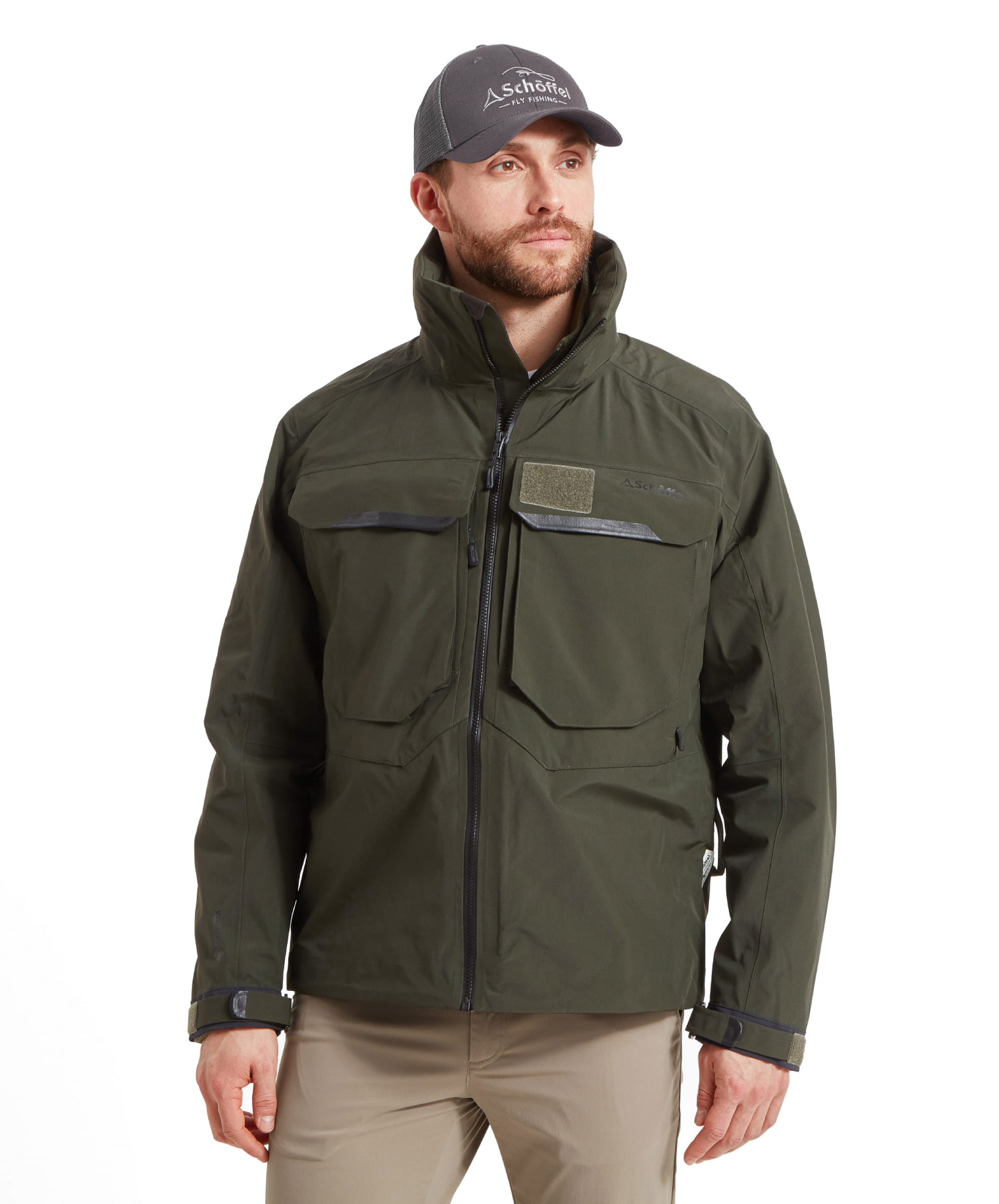 A man wears the Schöffel Salar II Wading Jacket for Men in Green with beige trousers and a grey Fly Fishing cap. He stands casually with his hands by his sides.