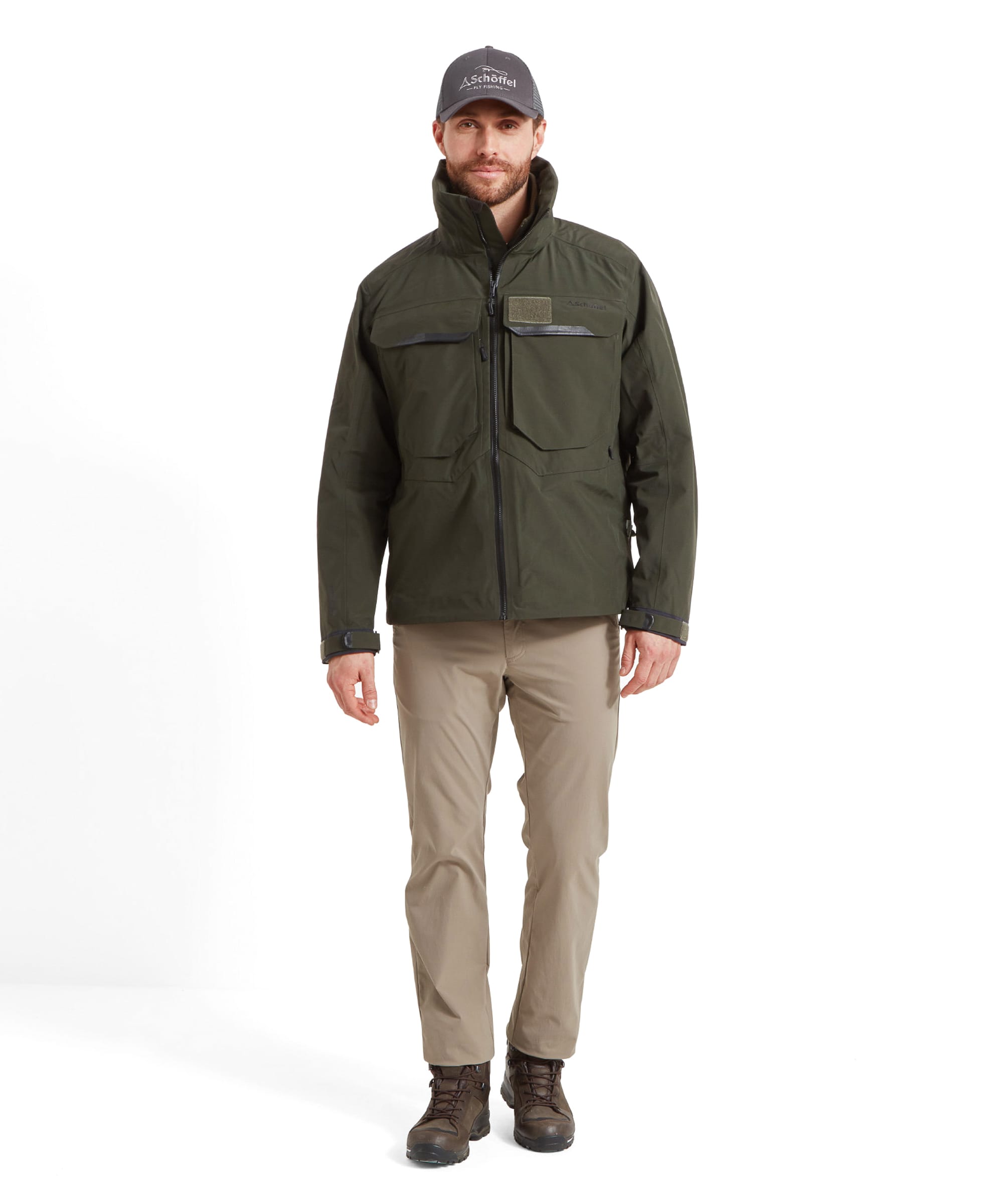 Full body view of a man wearing the Schöffel Salar II Wading Jacket for Men in Green with a grey cap, beige trousers and brown hiking boots. He's walking forward with a gentle smile.