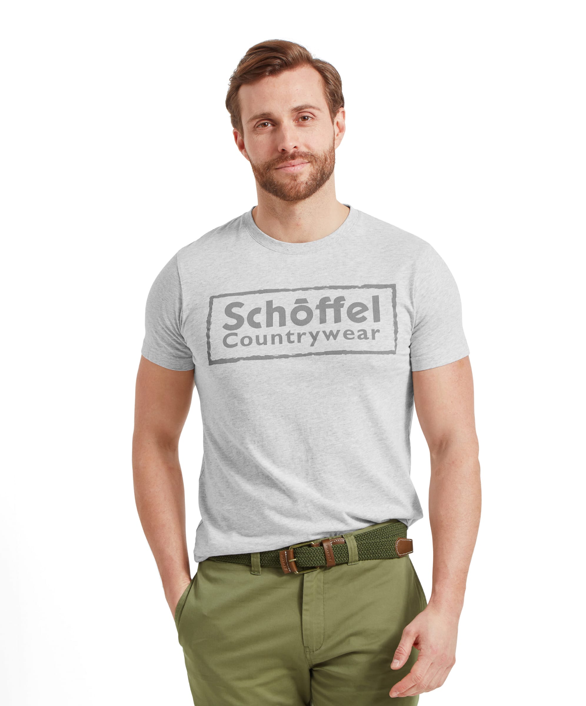 A man wears the Schöffel Heritage T-Shirt for Men in Grey with green trousers and a green woven belt. He stands casually with his left hand in his trouser pocket.