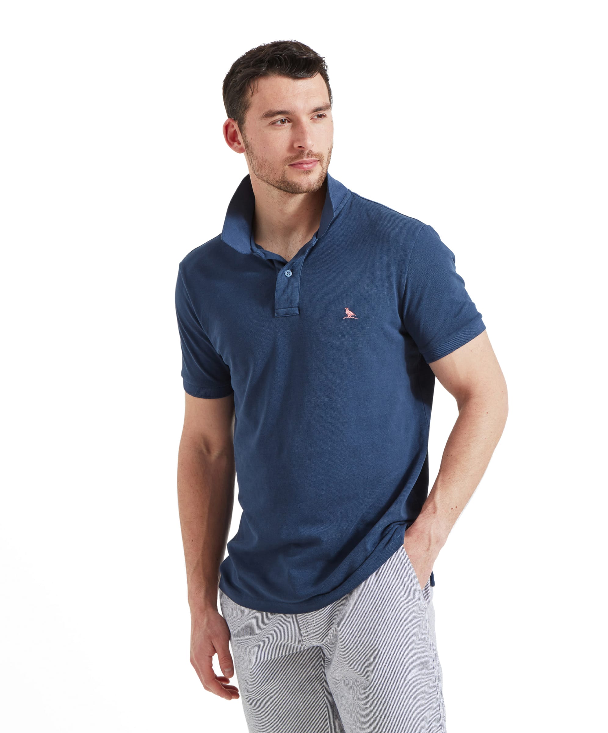 A man wears the Schöffel St Ives Garment Dyed Polo Shirt for Men in Blue with the collar popped up and styled with white and blue horizontal striped shorts.