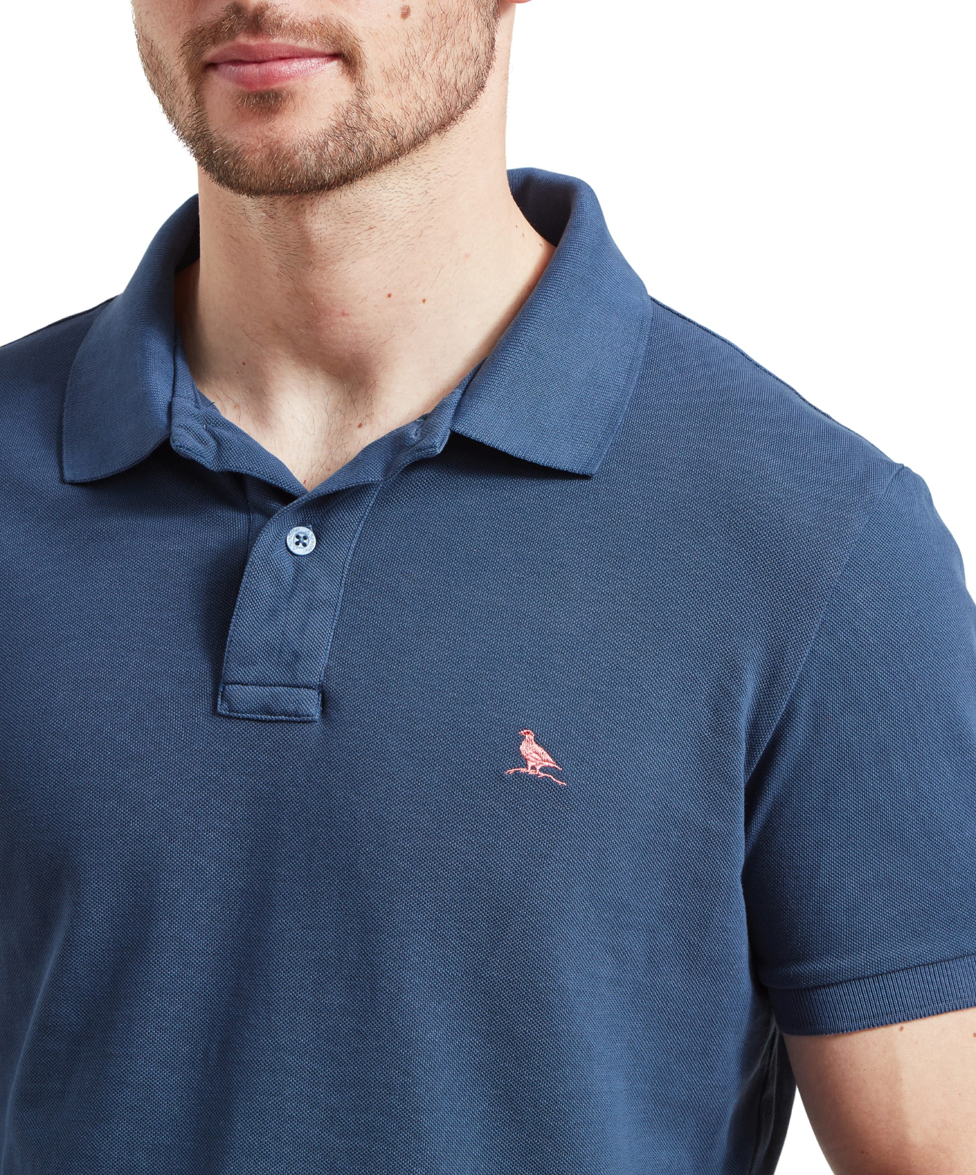 Close-up of the Schöffel St Ives Garment Dyed Polo Shirt for Men in Blue collar area which is worn slightly unbuttoned and a Ptarmigan can be seen embroidered onto the right chest in a pink thread.