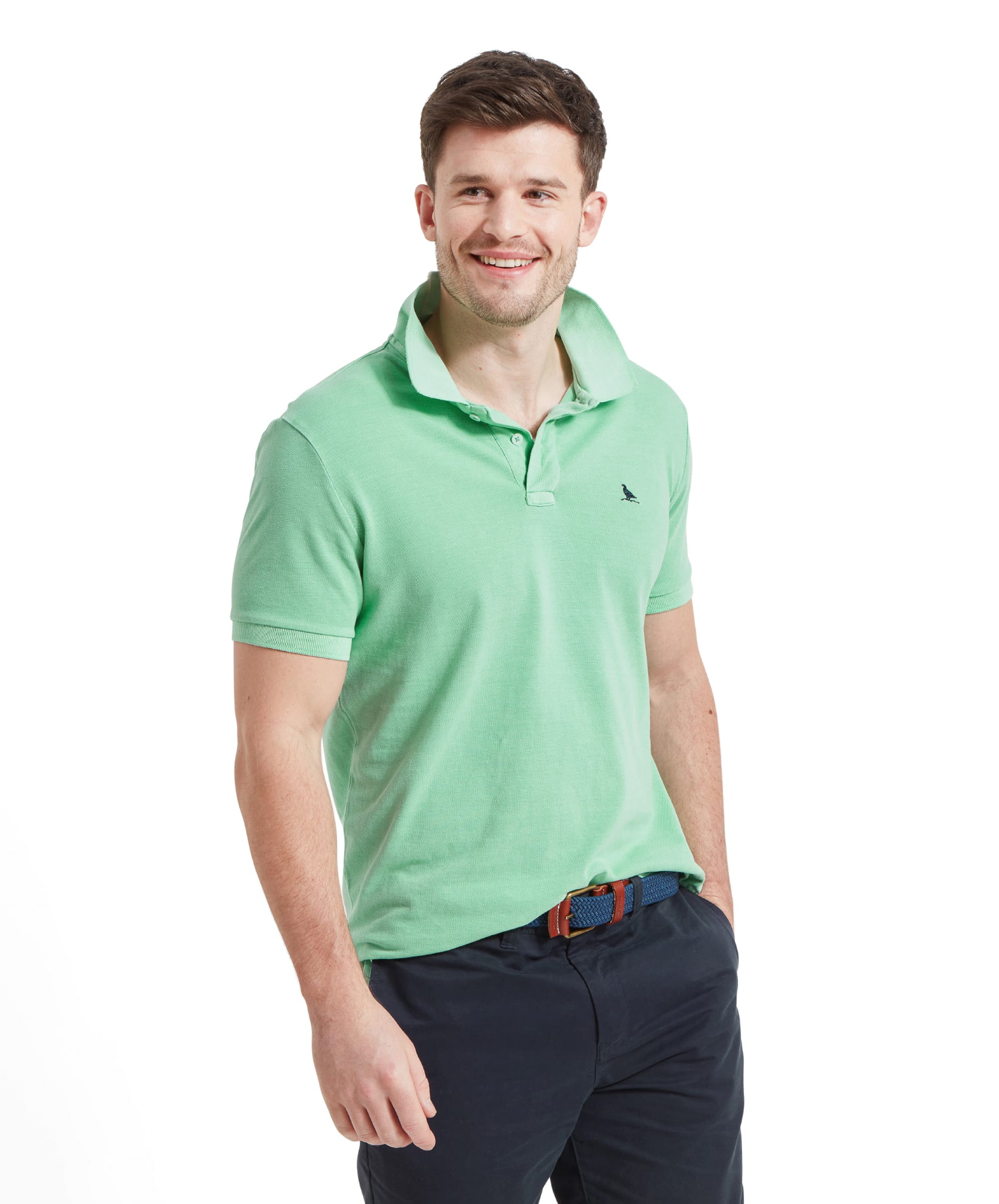 A man wears the Schöffel St Ives Garment Dyed Polo Shirt for Men in Green with the collar popped up and styles with navy shorts and a blue woven belt.