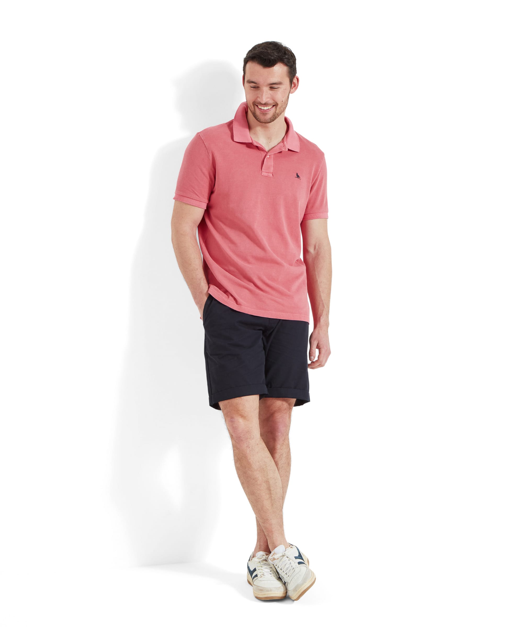 Full view of a man wearing the Schöffel St Ives Garment Dyed Polo Shirt for Men in Pink styled with navy chino shorts and white trainers.