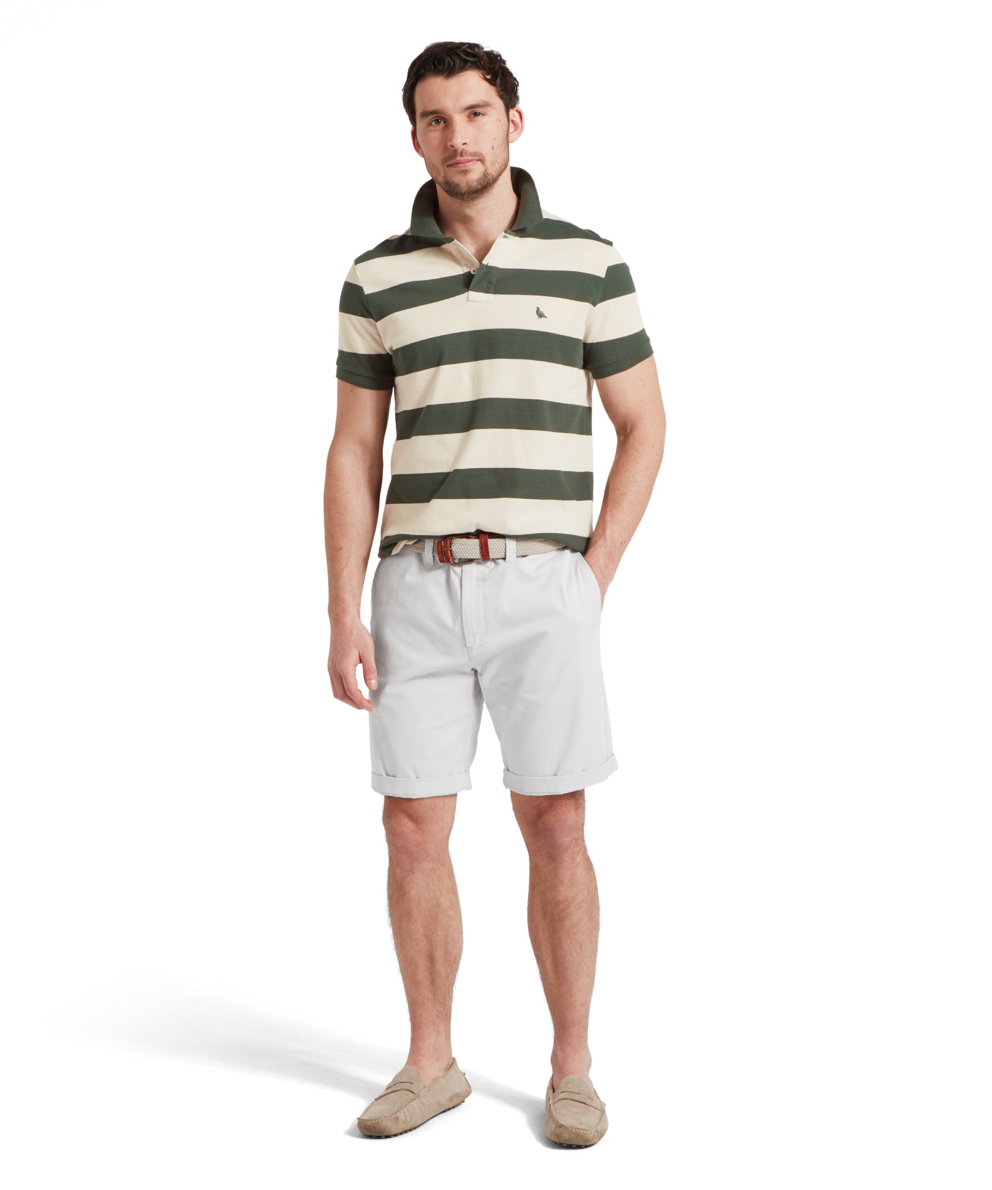 A full height image of a male model wearing a green and beige striped Schöffel polo shirt with a small embroidered bird logo on the chest, paired with light grey shorts. He is standing in a relaxed pose with one hand in his pocket.