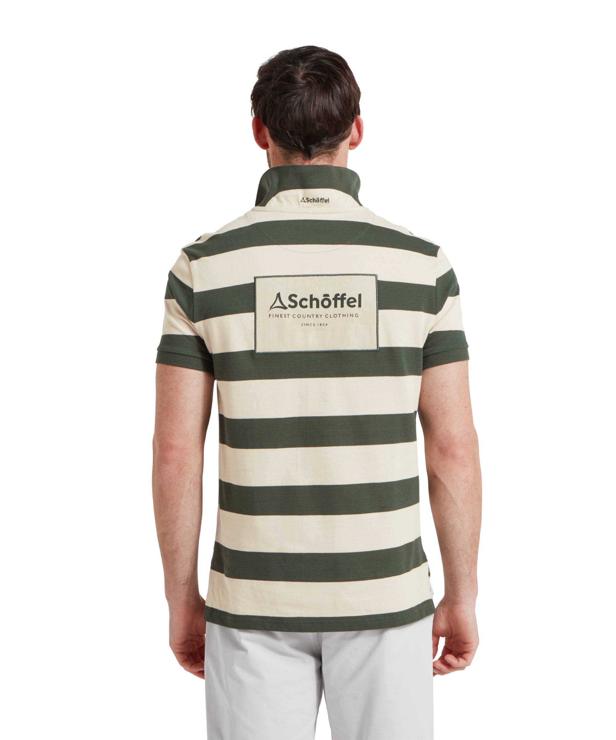 A back image of a male model wearing a green and beige striped Schöffel polo shirt with a large "Schöffel" logo on the back. It is paired with light grey shorts and he is standing in a relaxed pose with his hands by his side.