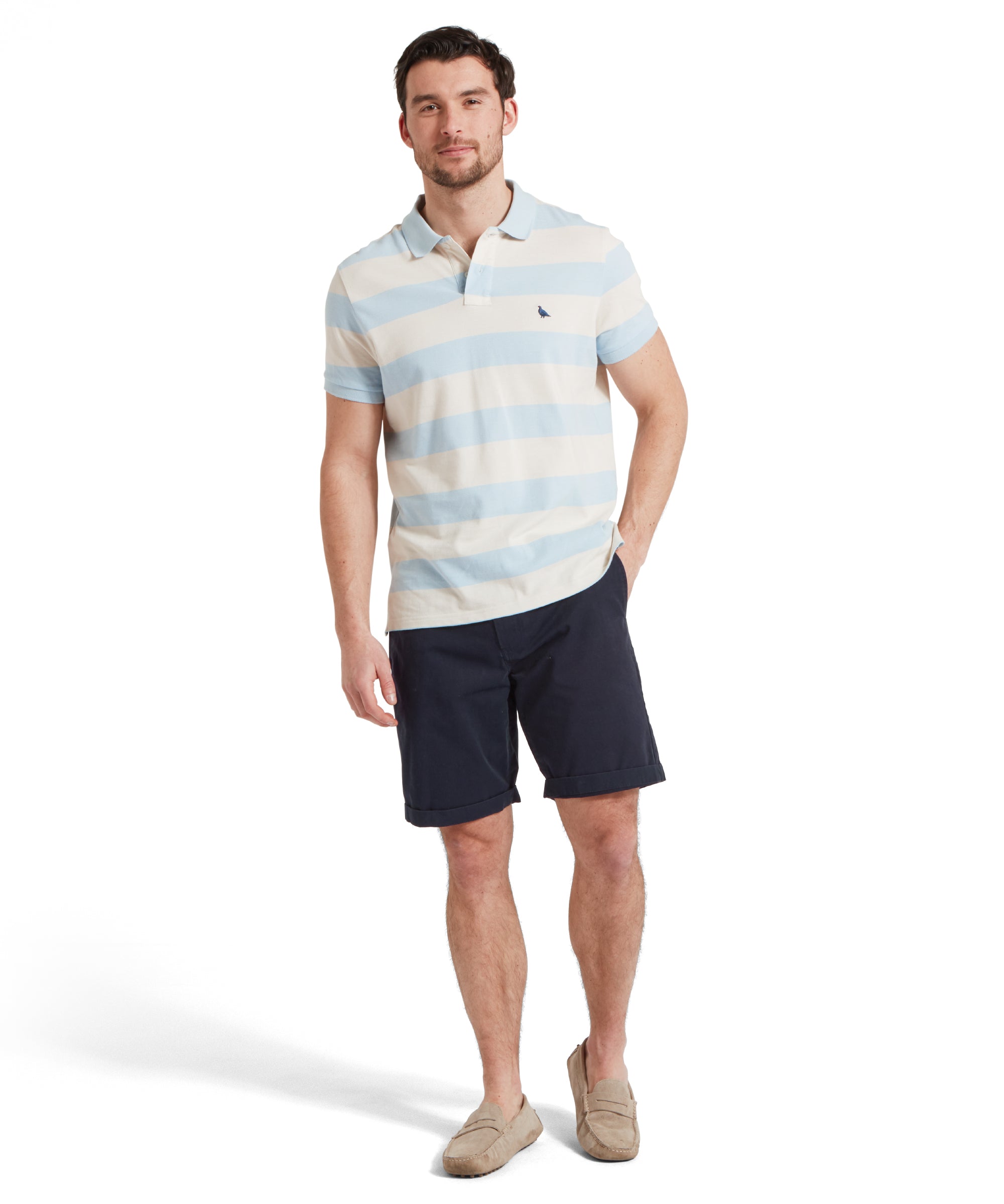 A full height image of a male model wearing a blue and beige striped Schöffel polo shirt with a small embroidered bird logo on the chest, paired with navy shorts and tan loafers. He is standing in a relaxed pose with one hand in his pocket.