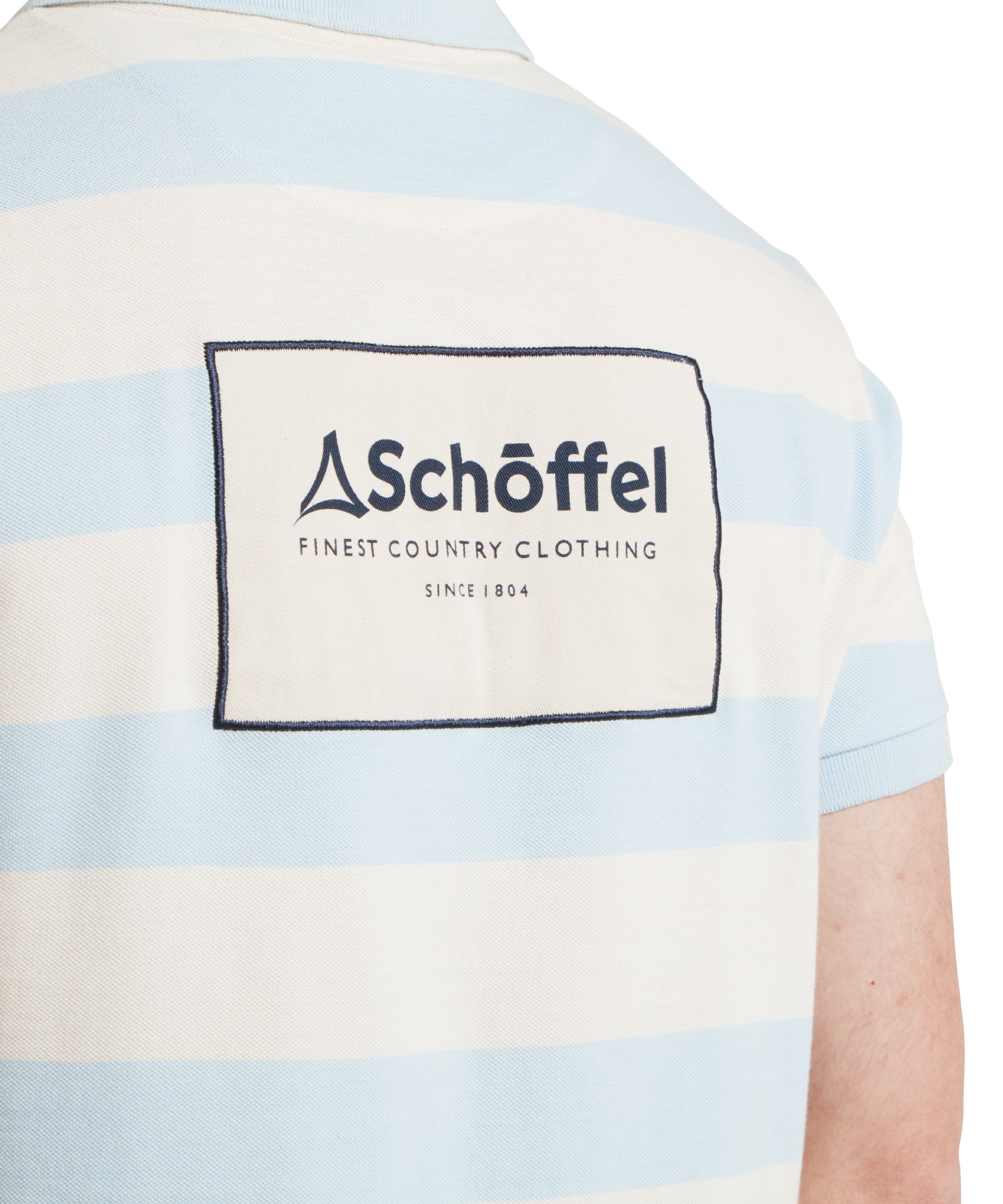 A close up image of a male model wearing a blue and beige striped Schöffel polo shirt with a large "Schöffel" logo on the back.