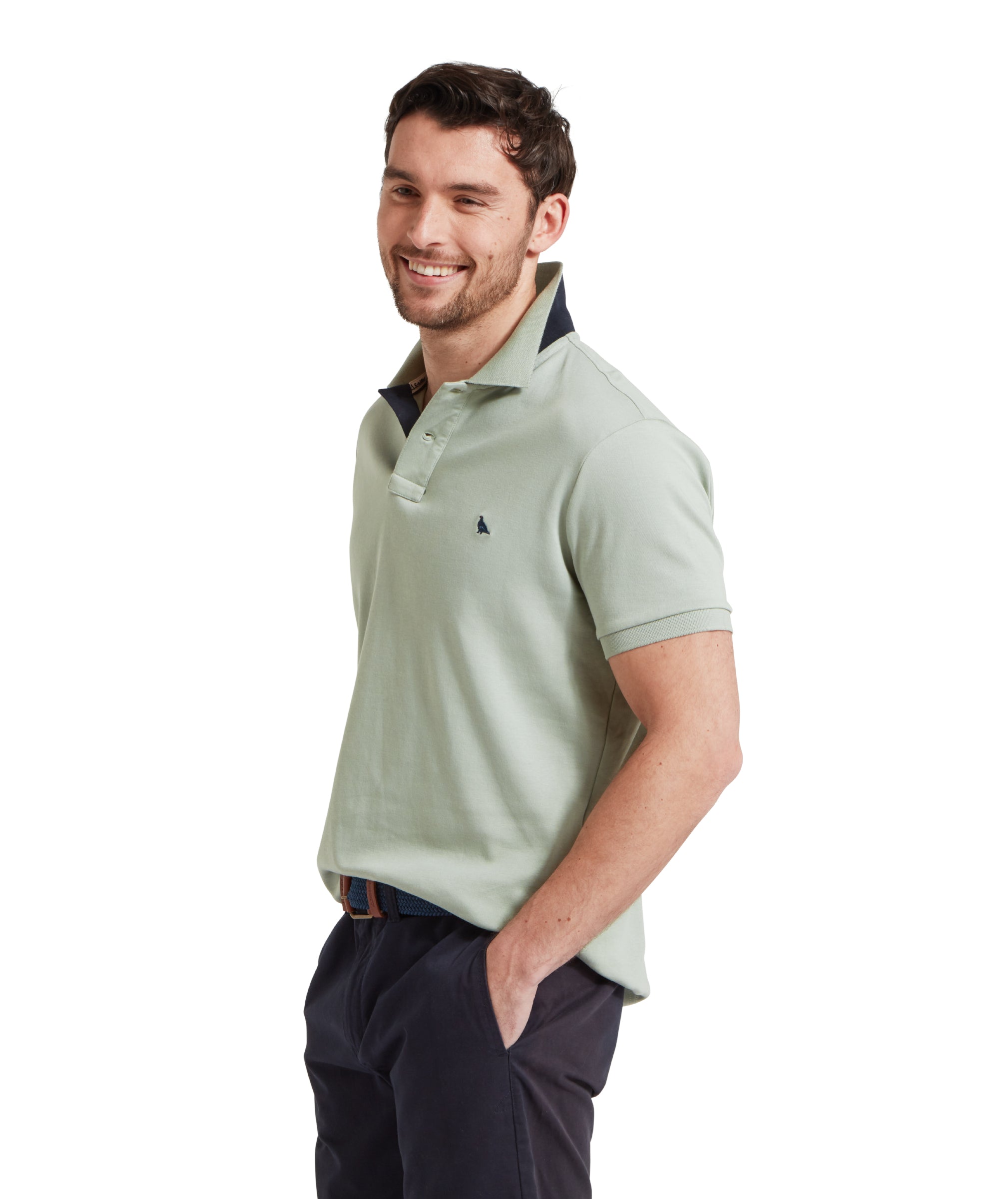 A side view image of a male model wearing a light green Schöffel t-shirt with a small embroidered bird logo on the chest, paired with navy shorts and a blue woven belt. He is standing in a relaxed pose with one hand in his pocket.