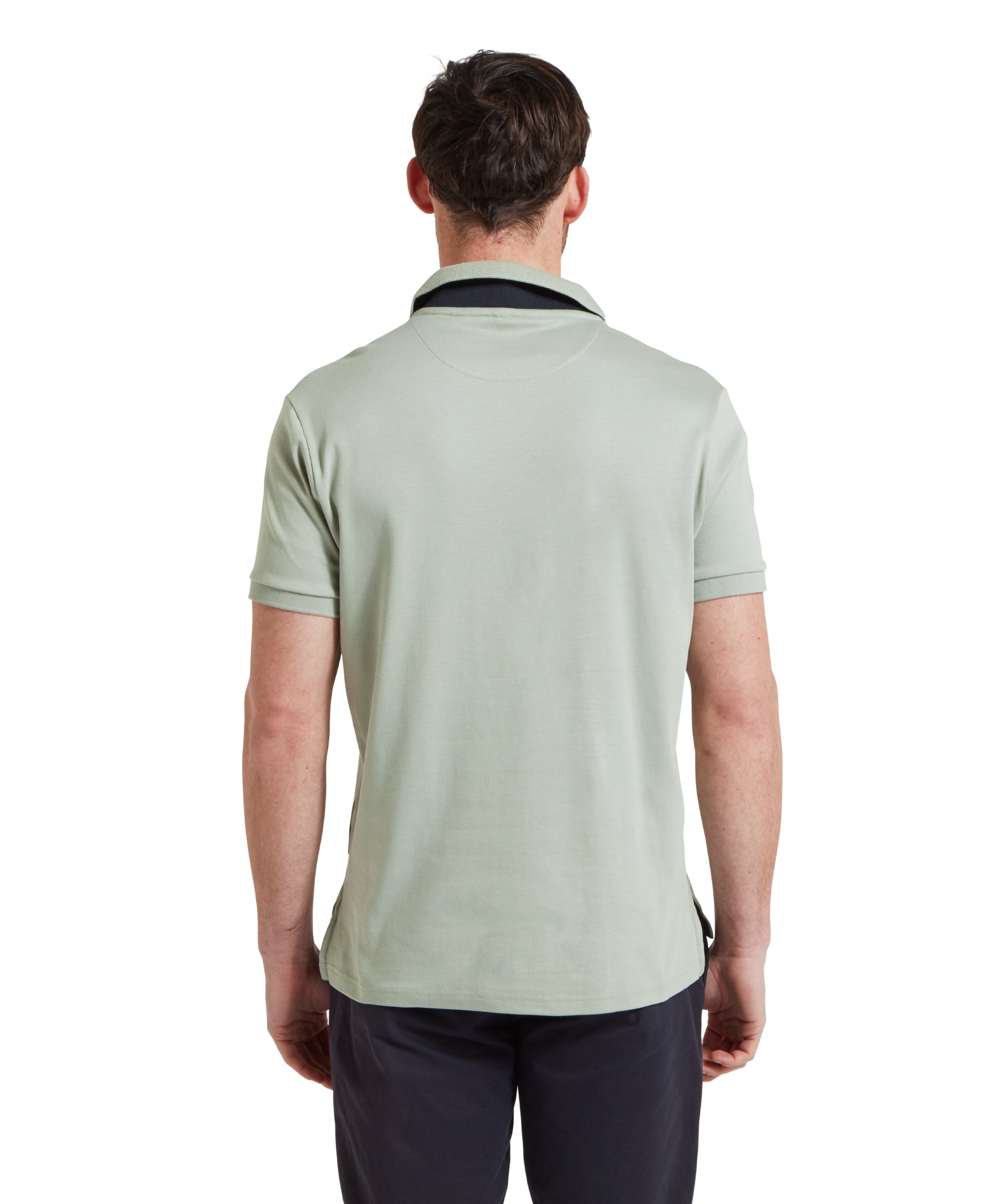 A back view image of a male model wearing a light green Schöffel t-shirt with a small embroidered bird logo on the chest, paired with navy shorts and a blue woven belt.