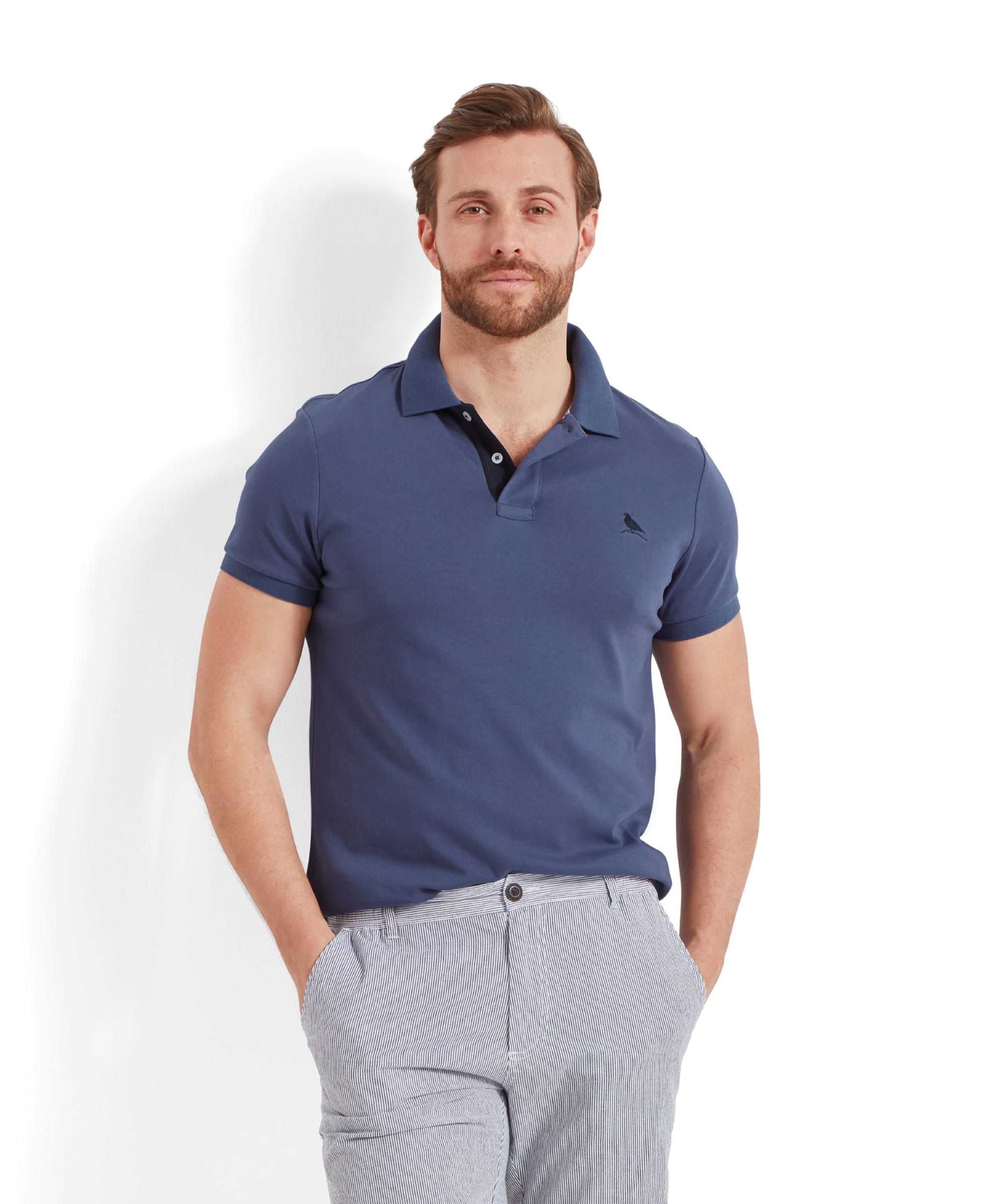 A man modeling the Schöffel St Ives Jersey Polo Shirt for Men in Blue, standing with hands in pockets. The shirt is a classic polo style with a pointed collar and button placket.