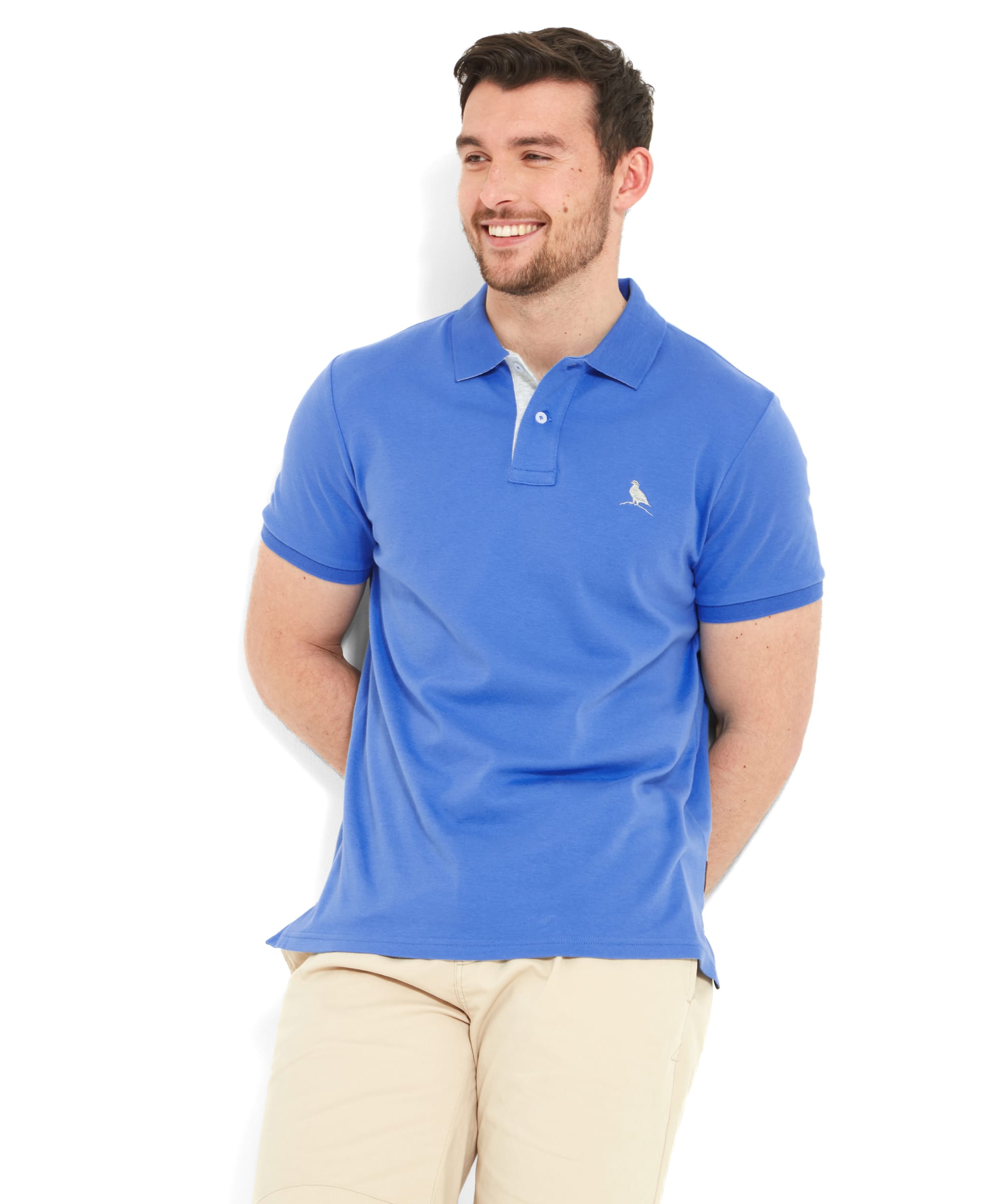 A man wearing the Schöffel Men's St Ives Jersey Polo Shirt in light blue, paired with beige shorts. The shirt features a small embroidered Ptarmigan logo on the left chest and has a classic polo collar.