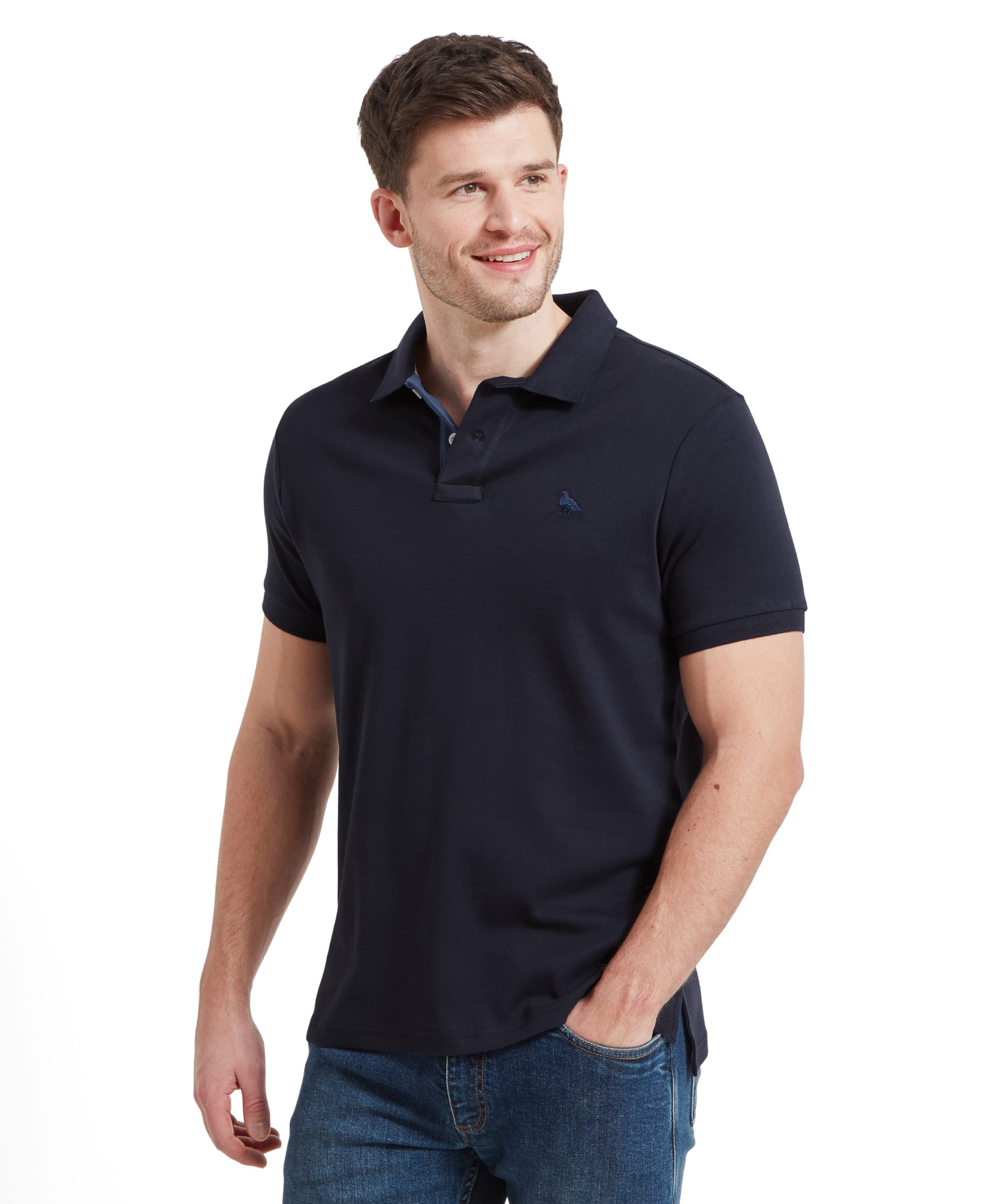 A man wearing the Schöffel Men's St Ives Jersey Polo Shirt in navy, paired with blue jeans. The shirt features a small embroidered bird logo on the left chest and has a classic polo collar.