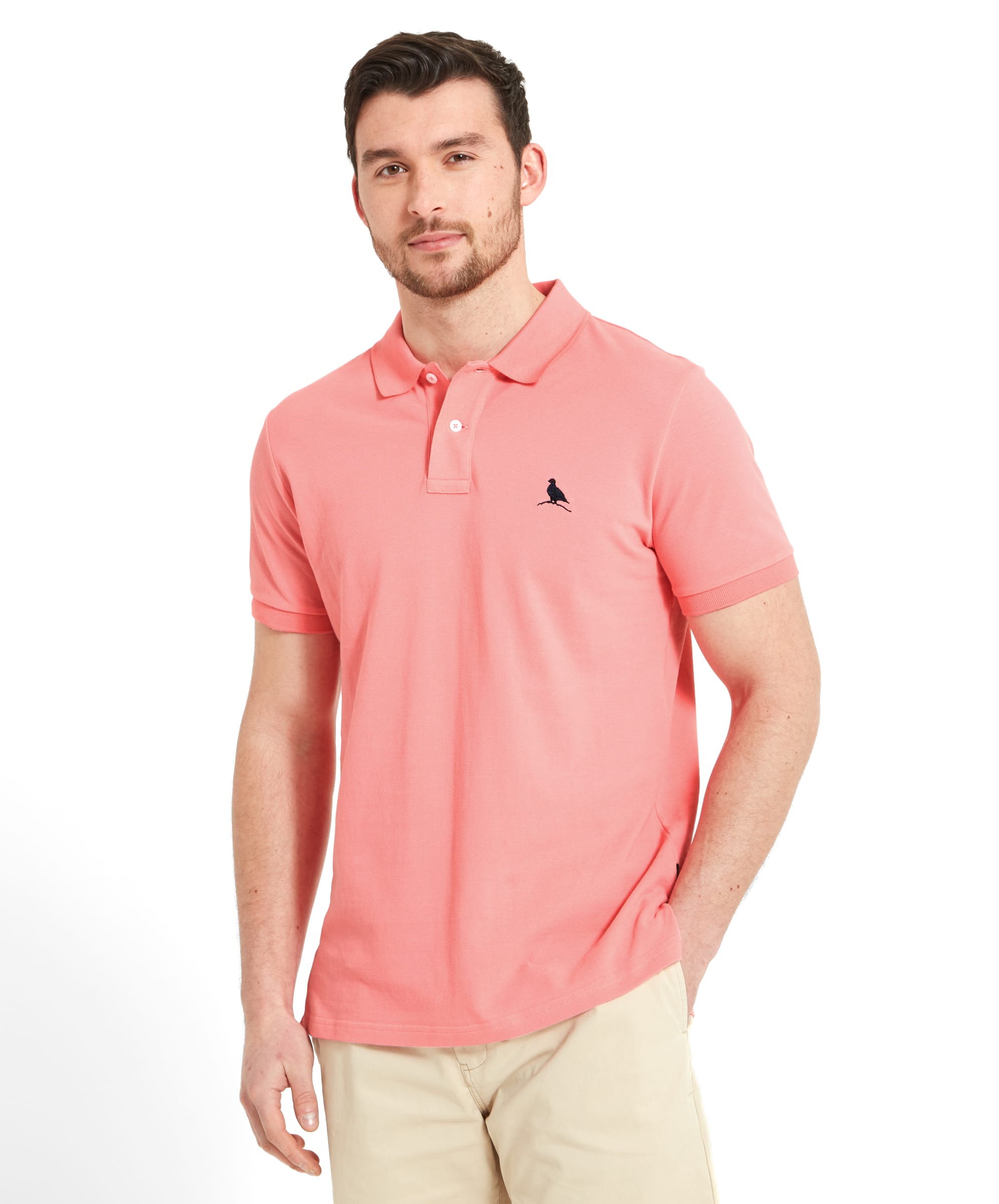 A man wearing the Schöffel St Ives Polo Shirt for Men in Pink, paired with beige shorts. The shirt features a small embroidered bird logo on the left chest and has a classic polo collar. The man stands with a relaxed posture, looking confidently at the camera.