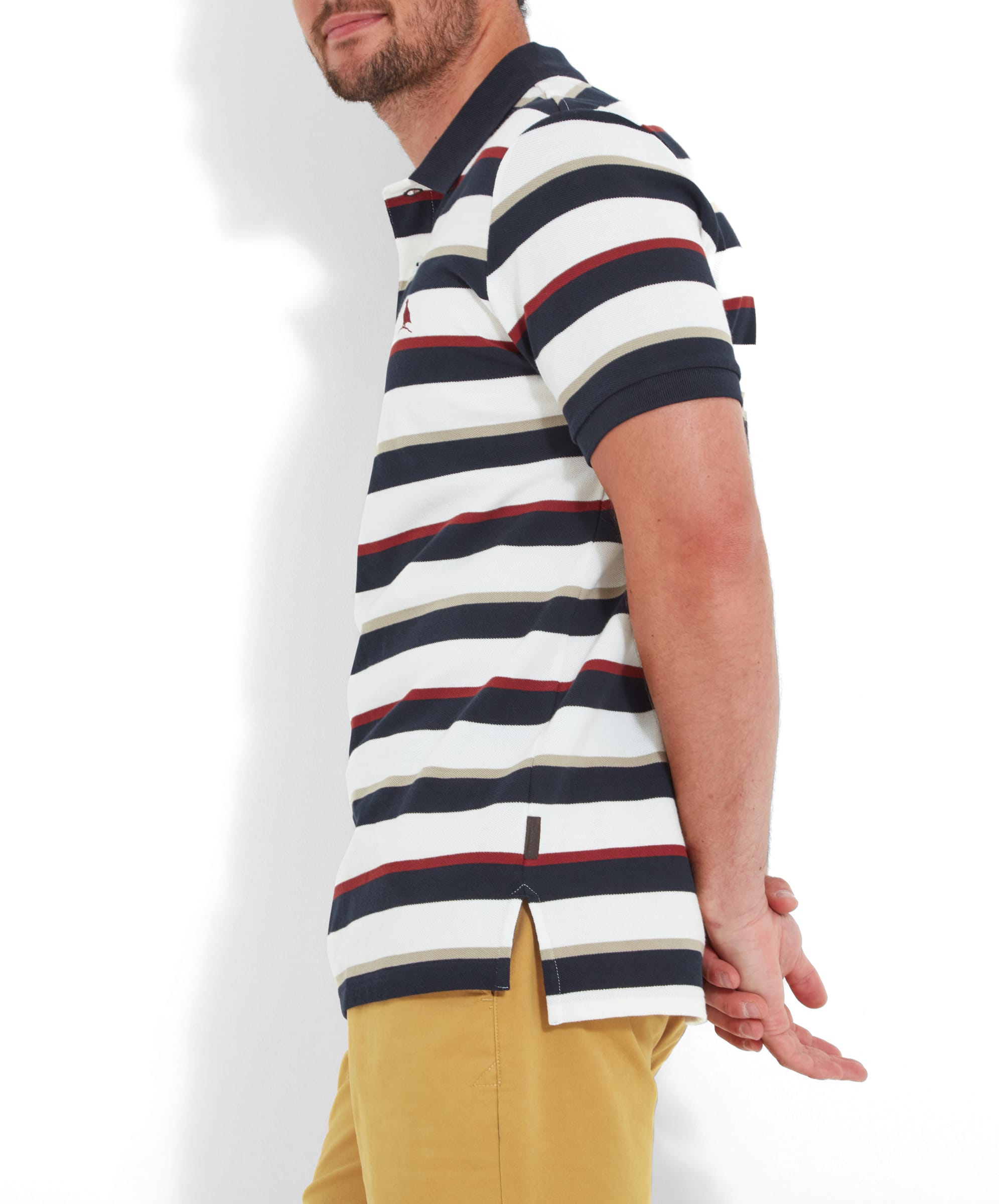 Side view of the man wearing the Schöffel St Ives Polo Shirt for Men in Red, showing the shirt's fit and the side slit detail. The combination of the stripes and the mustard yellow shorts adds a vibrant and playful touch to the outfit.