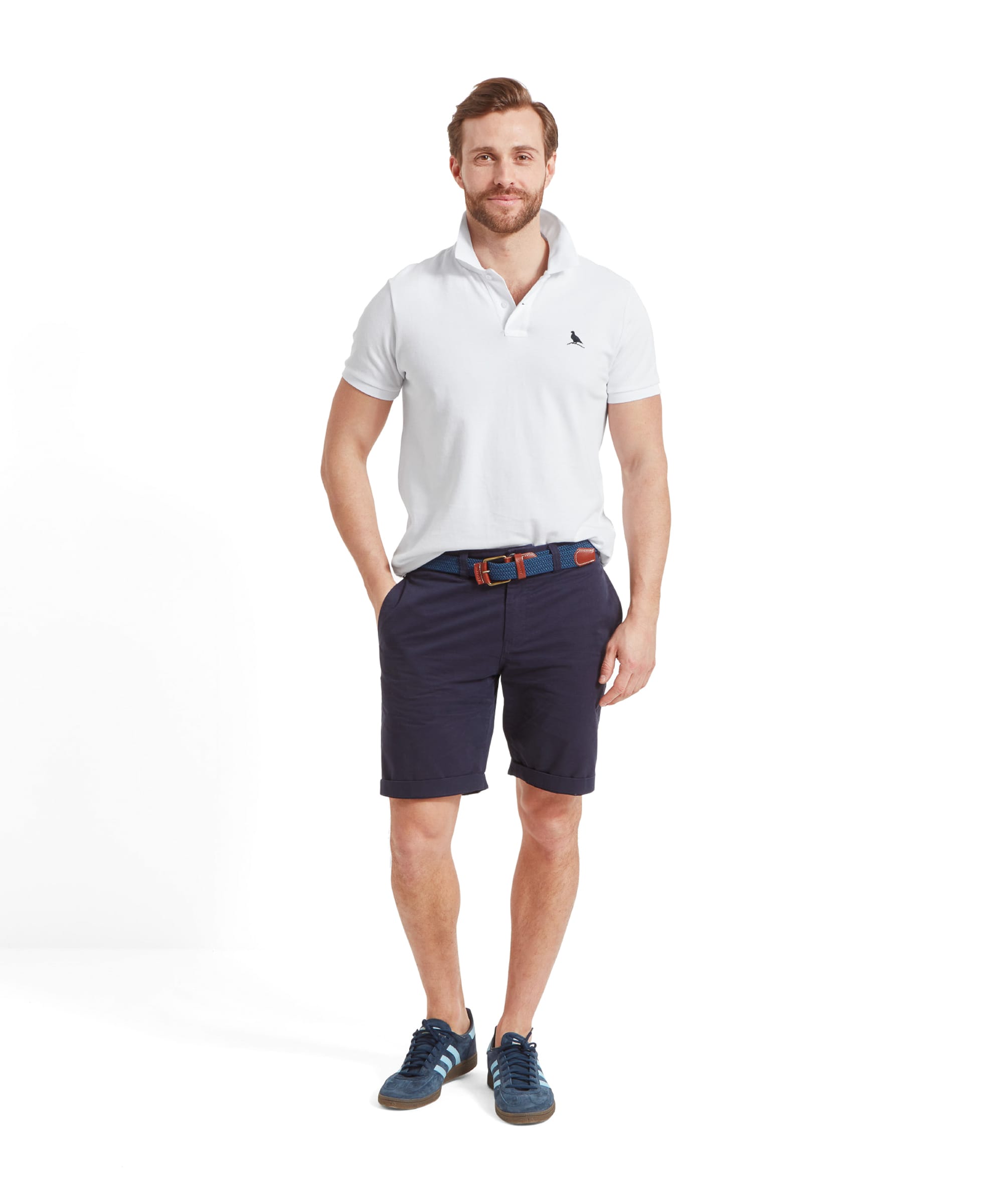 The same man in a Schöffel St Ives Polo Shirt for Men in White and navy shorts, standing with hands in pockets and smiling.