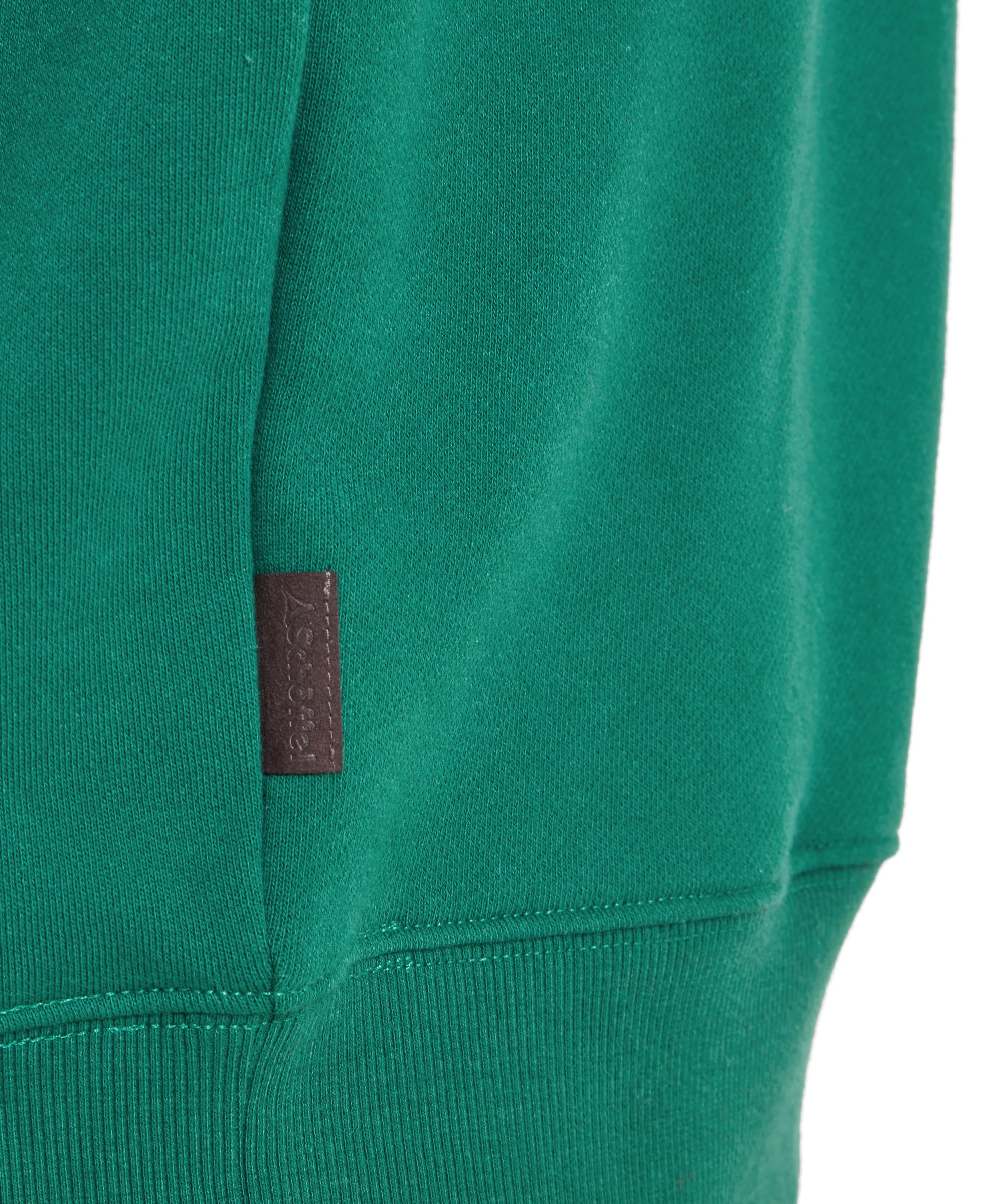 A close-up of the Schöffel St Merryn Sweatshirt for Men in Green’s hem and sleeve cuffs, showing the ribbed detailing and a small fabric tag on the side. The sweatshirt is worn with blue jeans.