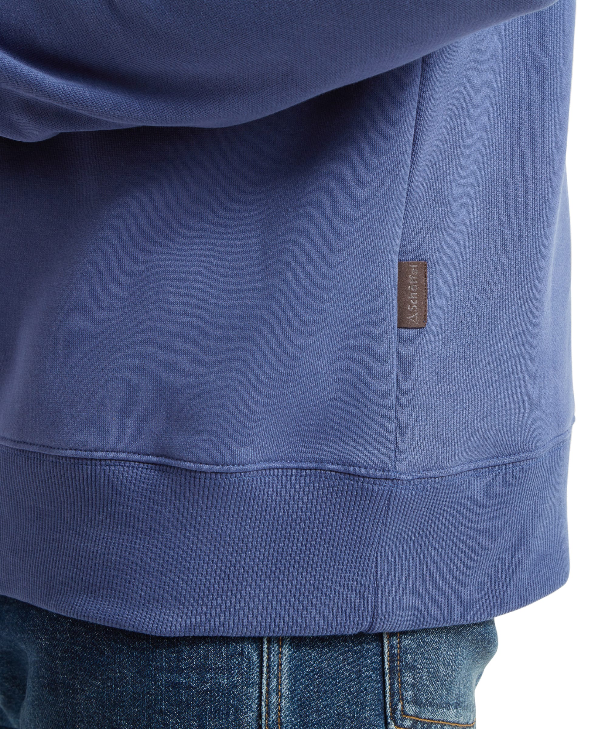 The final image focuses on the hem of the Schöffel St Merryn Sweatshirt for Men in Light Blue, where a small brand tag is stitched into the side seam, underscoring the brand's dedication to quality and style.