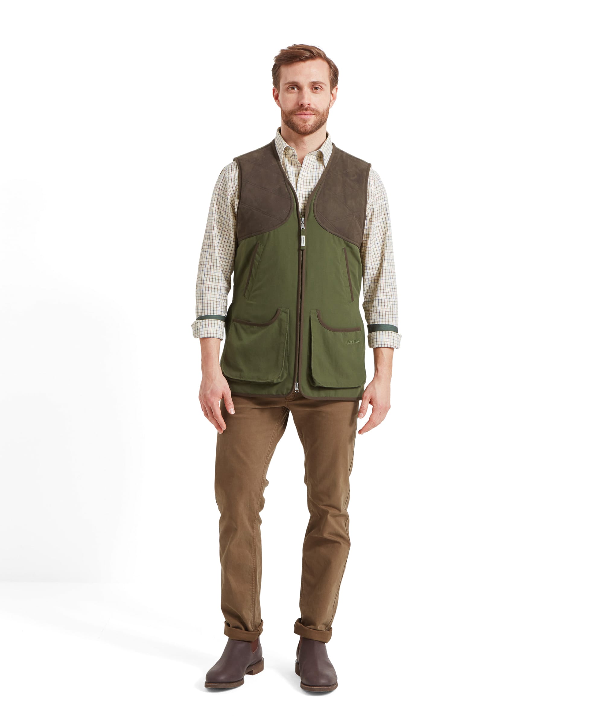 Full body view of a man modelling the Schöffel Stamford Vest II for Men in Green wearing it with a chream check shirt with the sleeves rolled up casually. He wears brown trousers and dark brown boots.