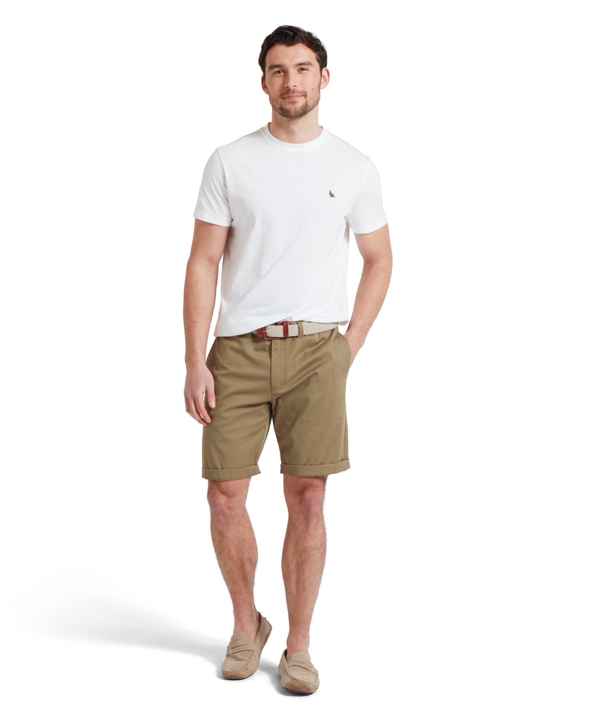 Male model standing in a relaxed pose, wearing a white Schöffel t-shirt with a small embroidered bird logo on the chest, khaki shorts, a woven belt, and beige loafers.