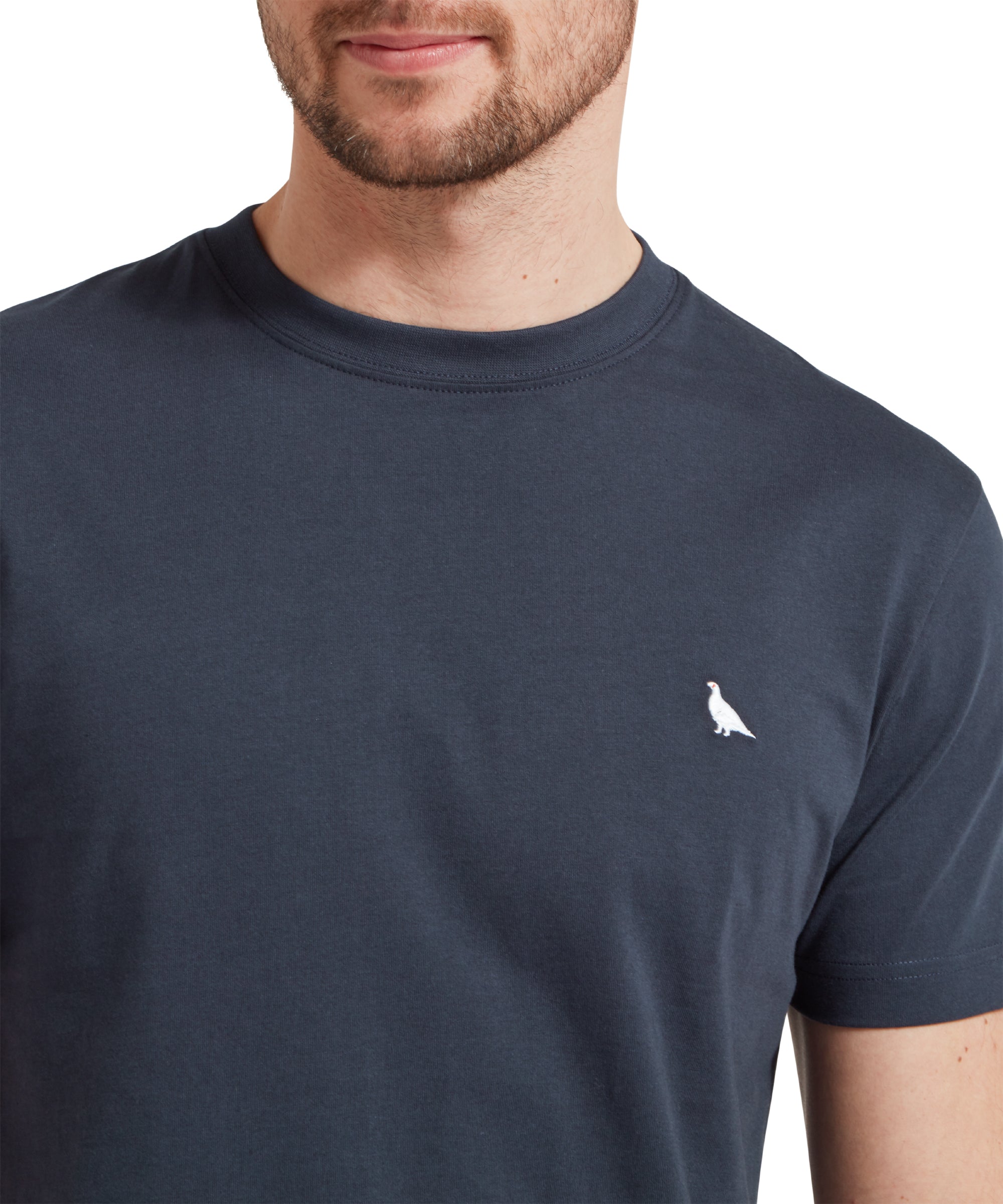 Close up of a male model wearing a navy Schöffel t-shirt with a white embroidered bird logo on the chest. The image highlights the white logo.