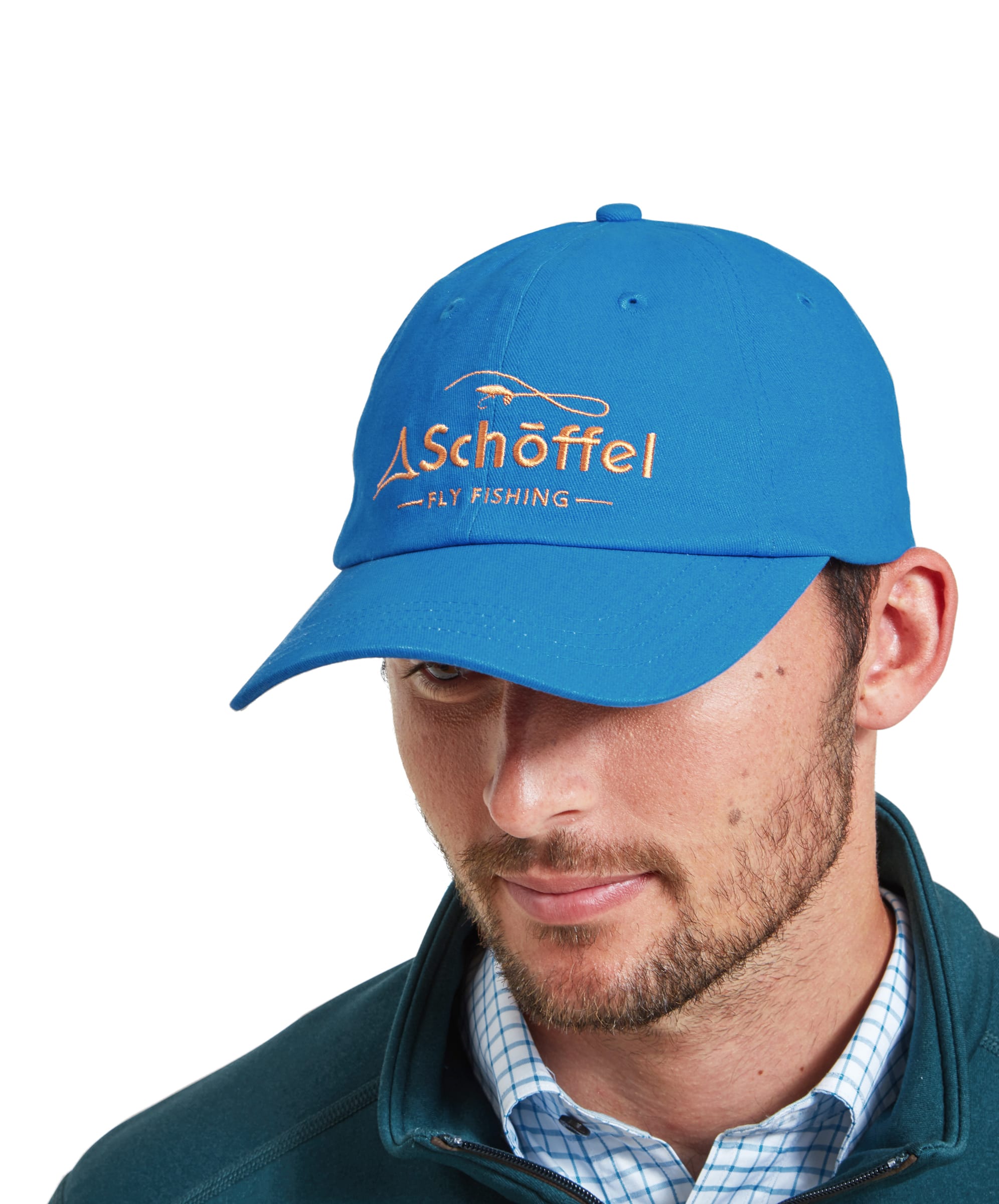 A man wears the Schöffel Tamar Fly Fishing Cap for Men in Blue partnered with a teal zip sweatshirt and a check shirt. To the front of the cap the Schöffel Fly Fishing branding can be seen in orange embroidery.