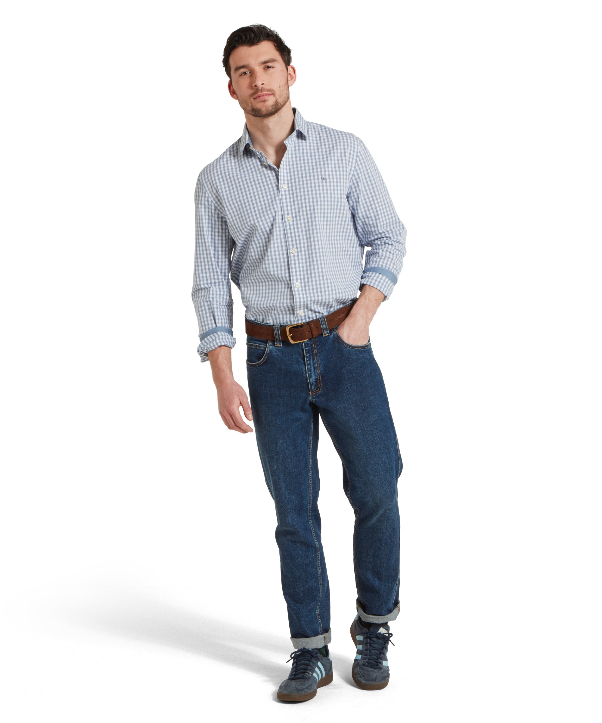 A man in the Schöffel Thorpeness Tailored Shirt for Men in Blue, standing casually with one hand in his pocket. He is wearing navy trainers, and dark denim jeans.