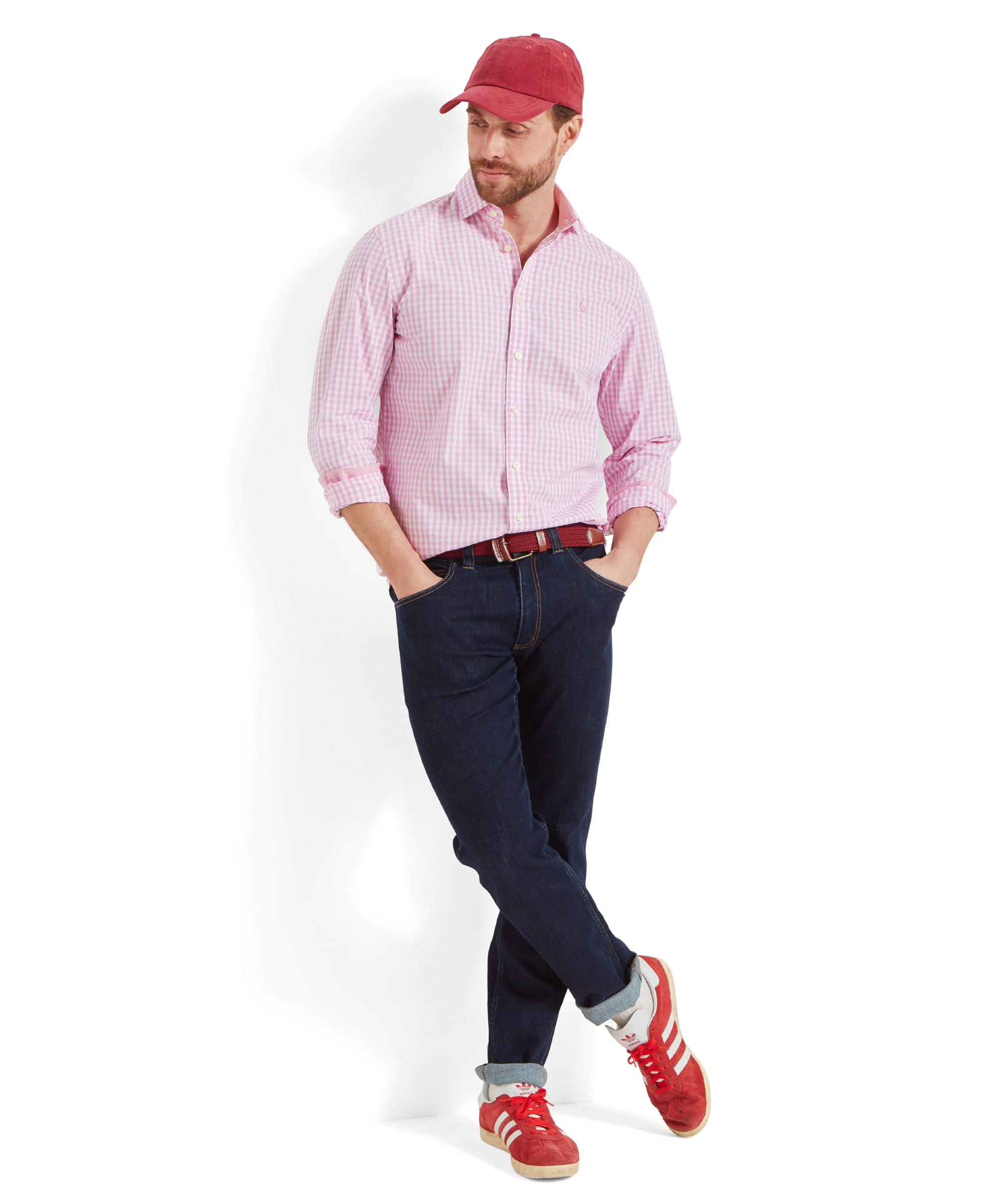 The same man in the Schöffel Thorpeness Tailored Shirt for Men in Pink and red cap, standing casually with one leg crossed over the other. He is wearing red trainers, adding a pop of color to the outfit.