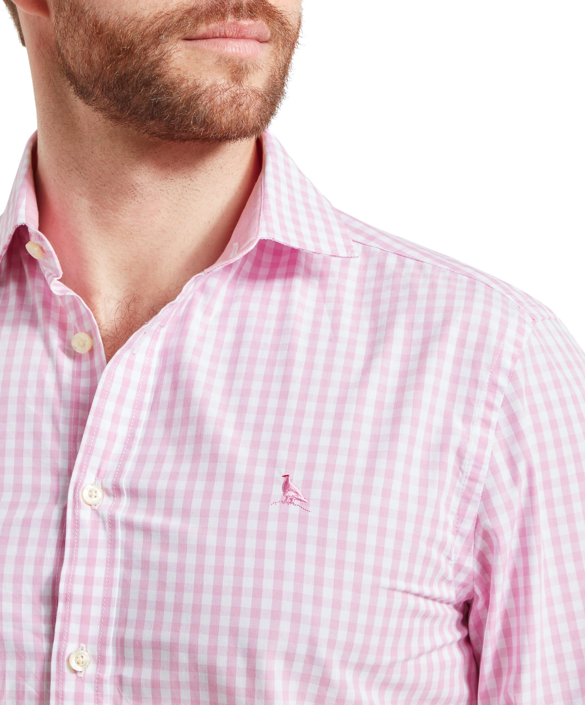 A close-up of the Schöffel Thorpeness Tailored Shirt for Men in Pink, focusing on the embroidered bird logo on the left chest. The man is wearing a red cap and has a light beard, adding to the casual, relaxed style.