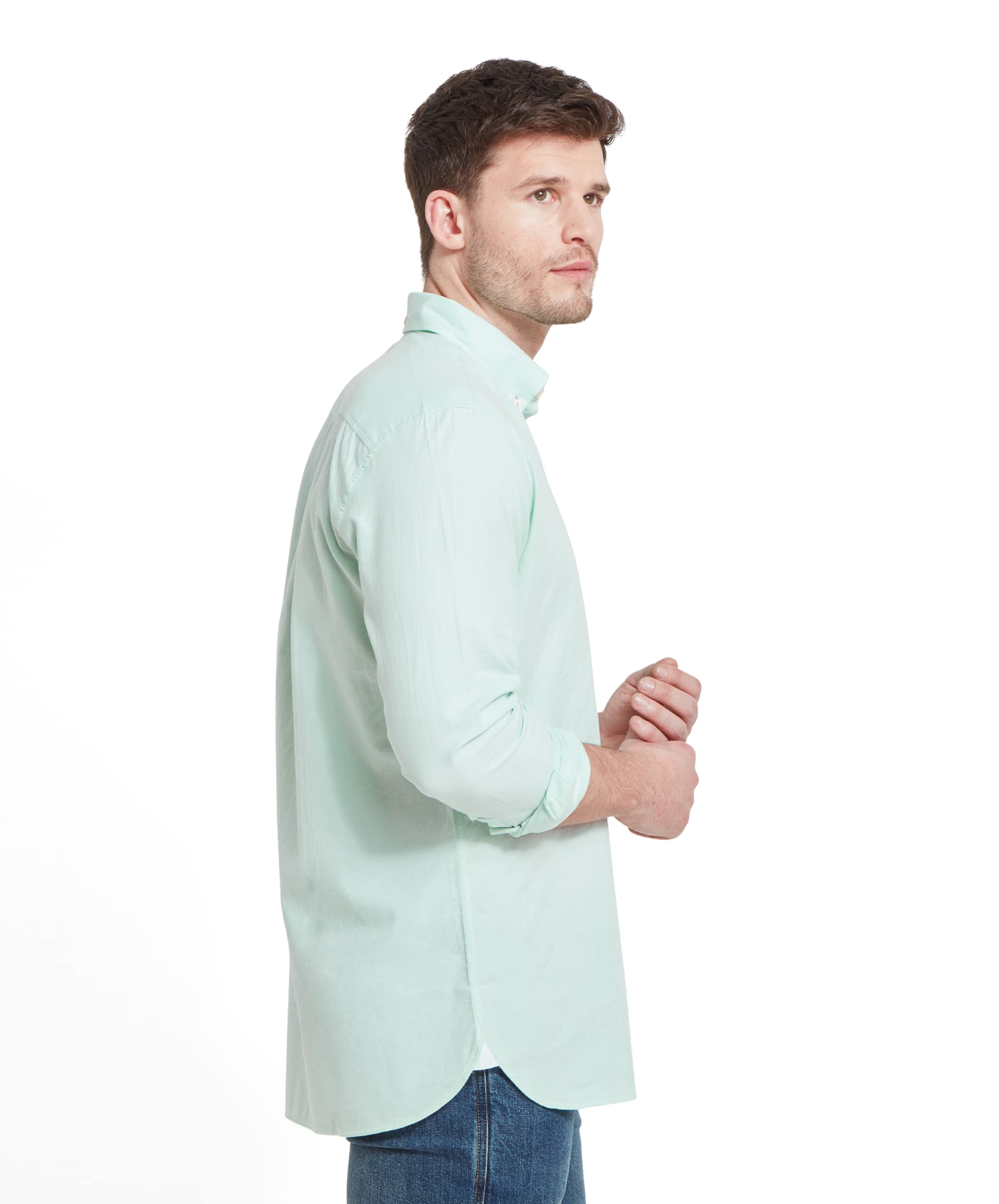 Side view of the man wearing the Schöffel Titchwell Tailored Shirt for Men in Green, looking towards the camera. The shirt is long and untucked, with the sleeves rolled up.