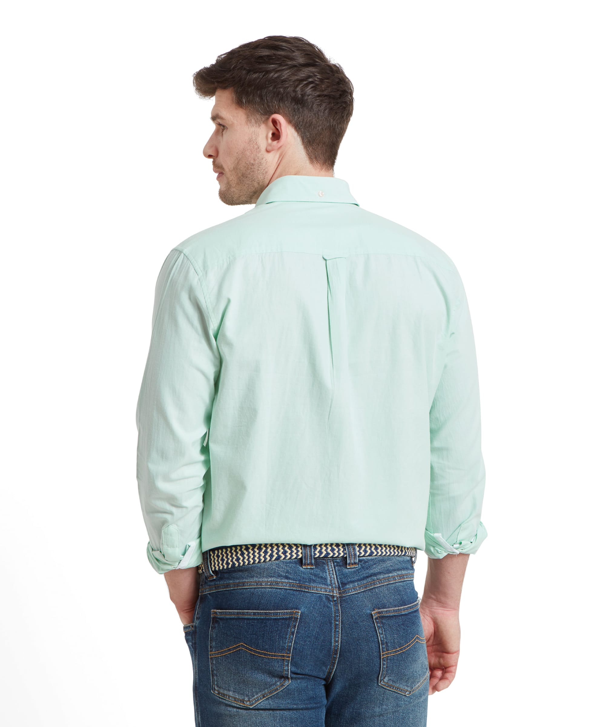 The man is shown from the back, highlighting the shirt's simple design. The shirt is Schöffel Titchwell Tailored Shirt for Men in Green, worn over blue jeans, with the sleeves rolled up.